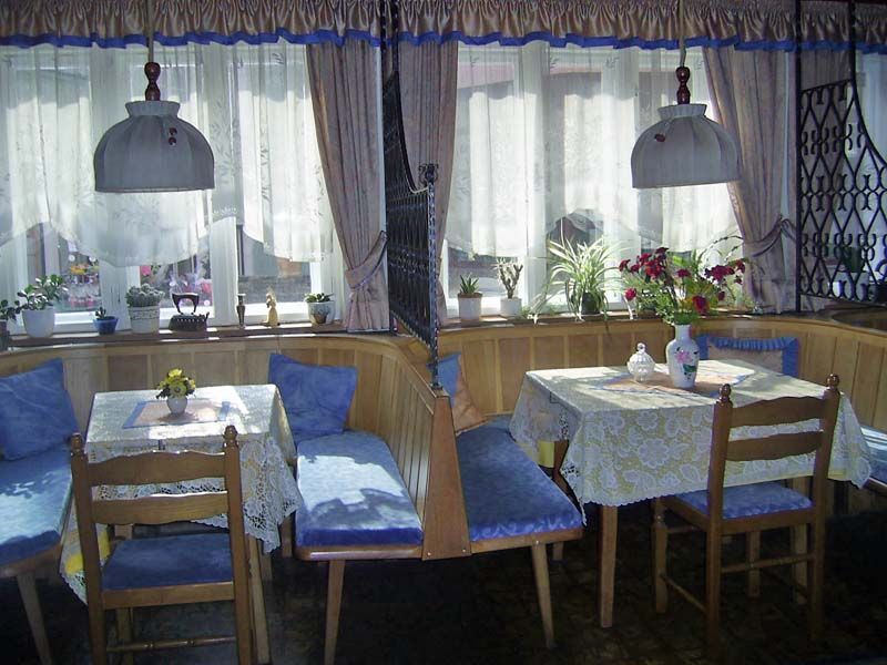 Cozy breakfast room with wooden furniture and blue upholstery, decorated with plants and flowers.