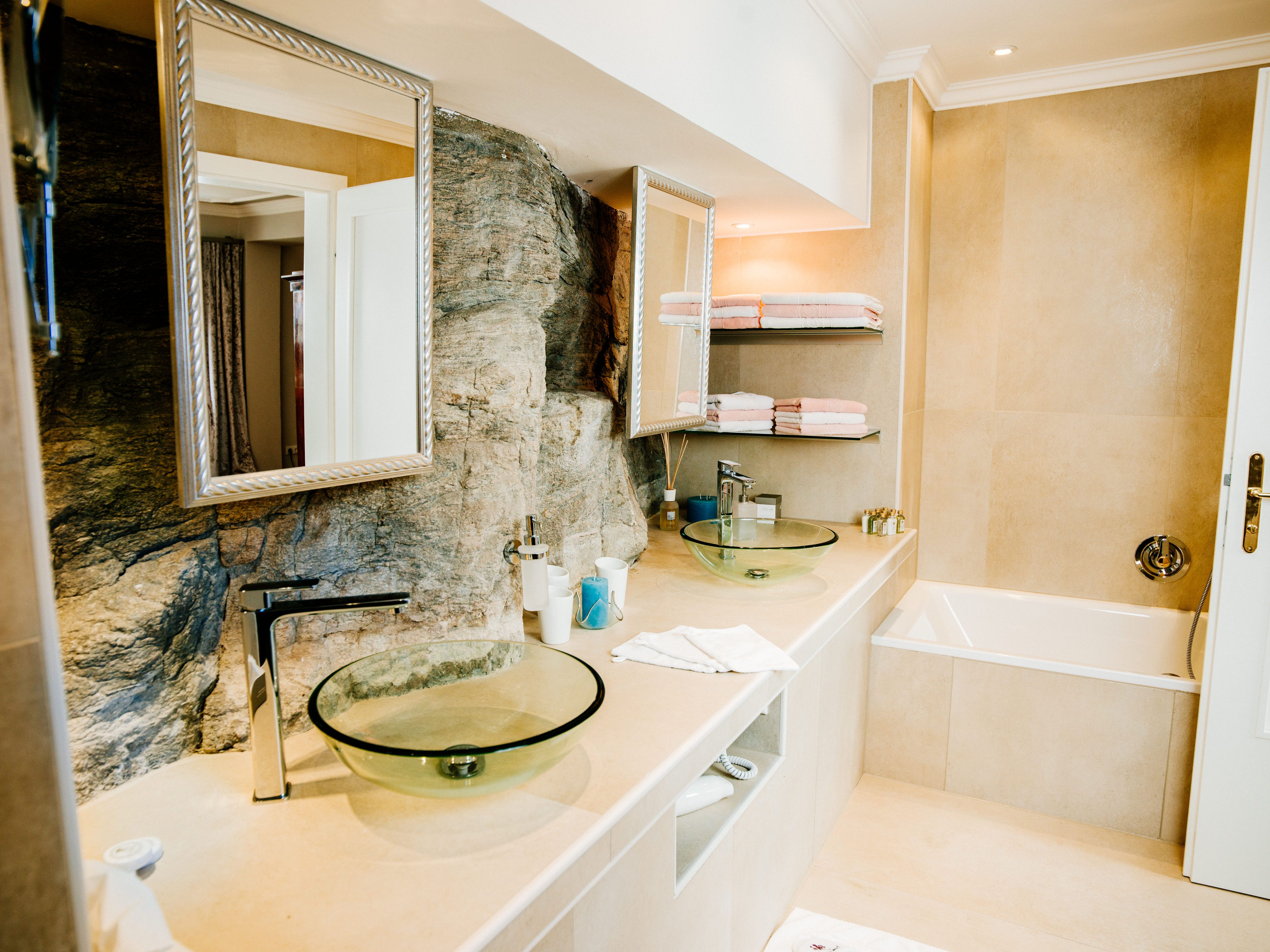 Modern bathroom with glass washbasin and natural stone wall.