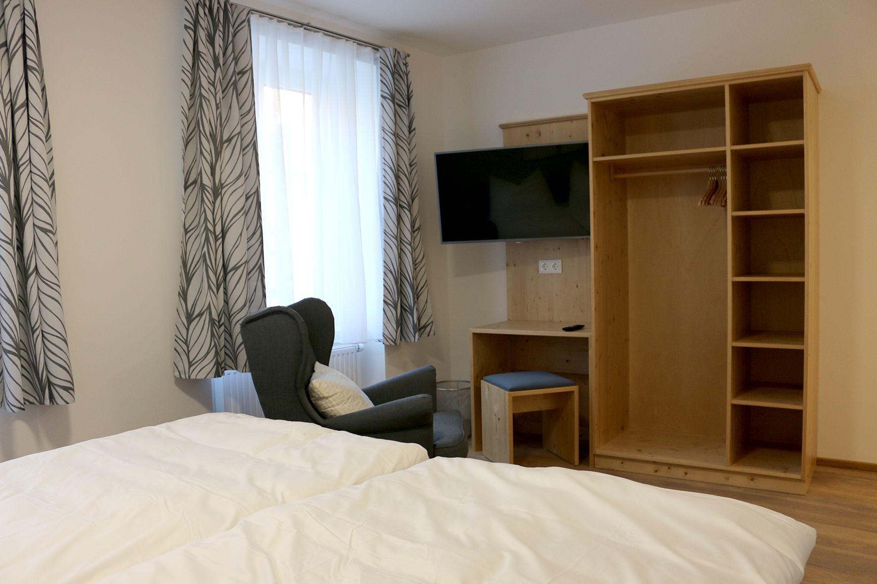 Open closet with TV on the wall. In front of a window with a curtain is a cozy green chair. 