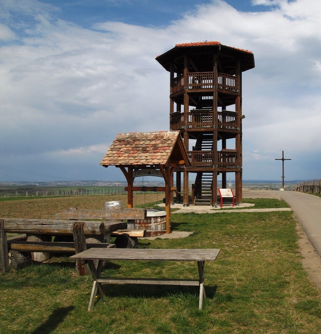 Wooden observation tower on a meadow with benches and a cross in the background.