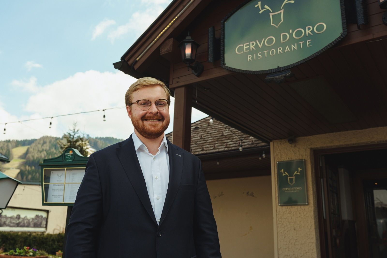 A man in a suit stands smiling in front of the Cervo D'Oro restaurant.