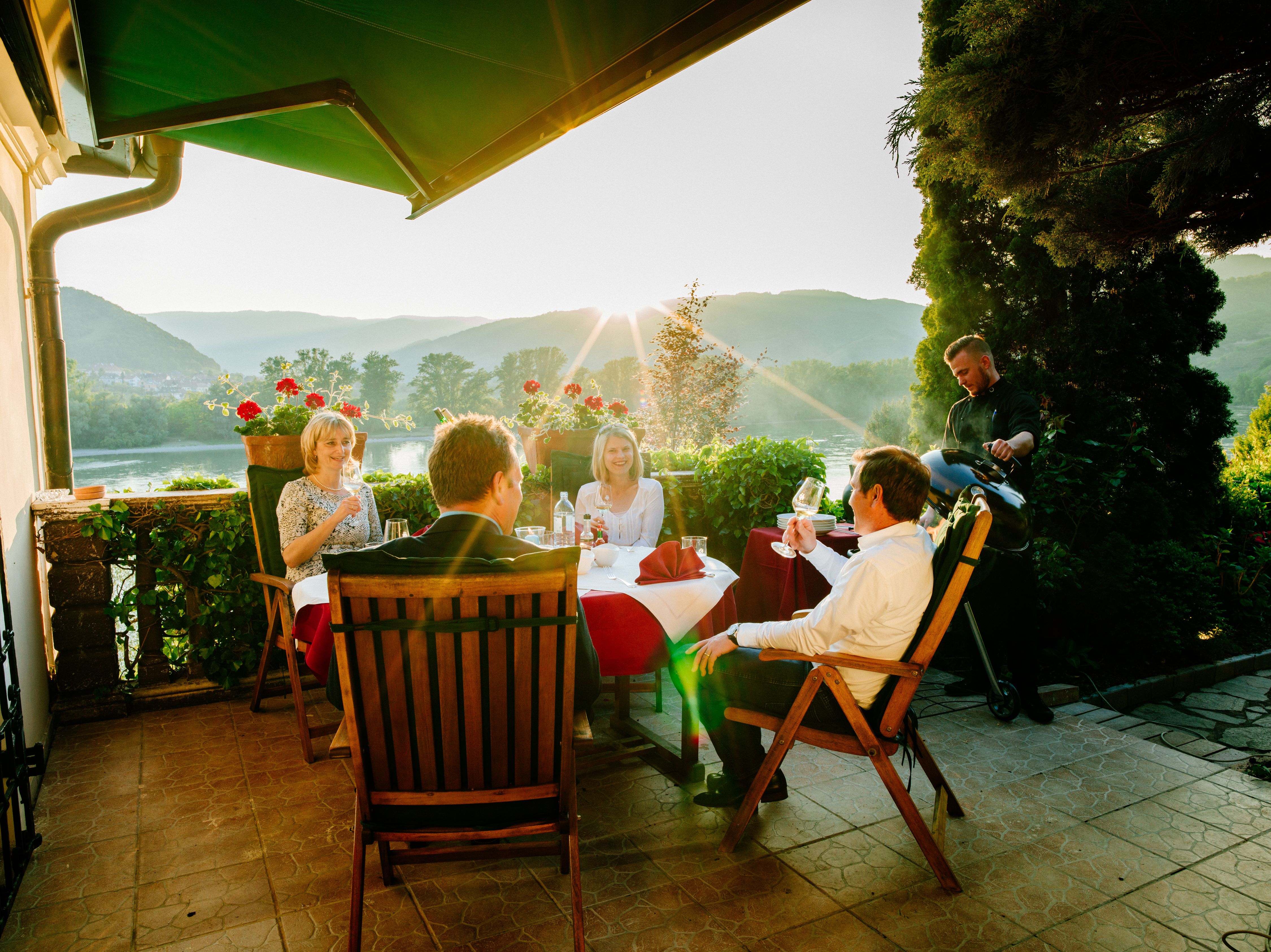 People sit on a terrace with a view of the mountains and enjoy a sunset dinner.