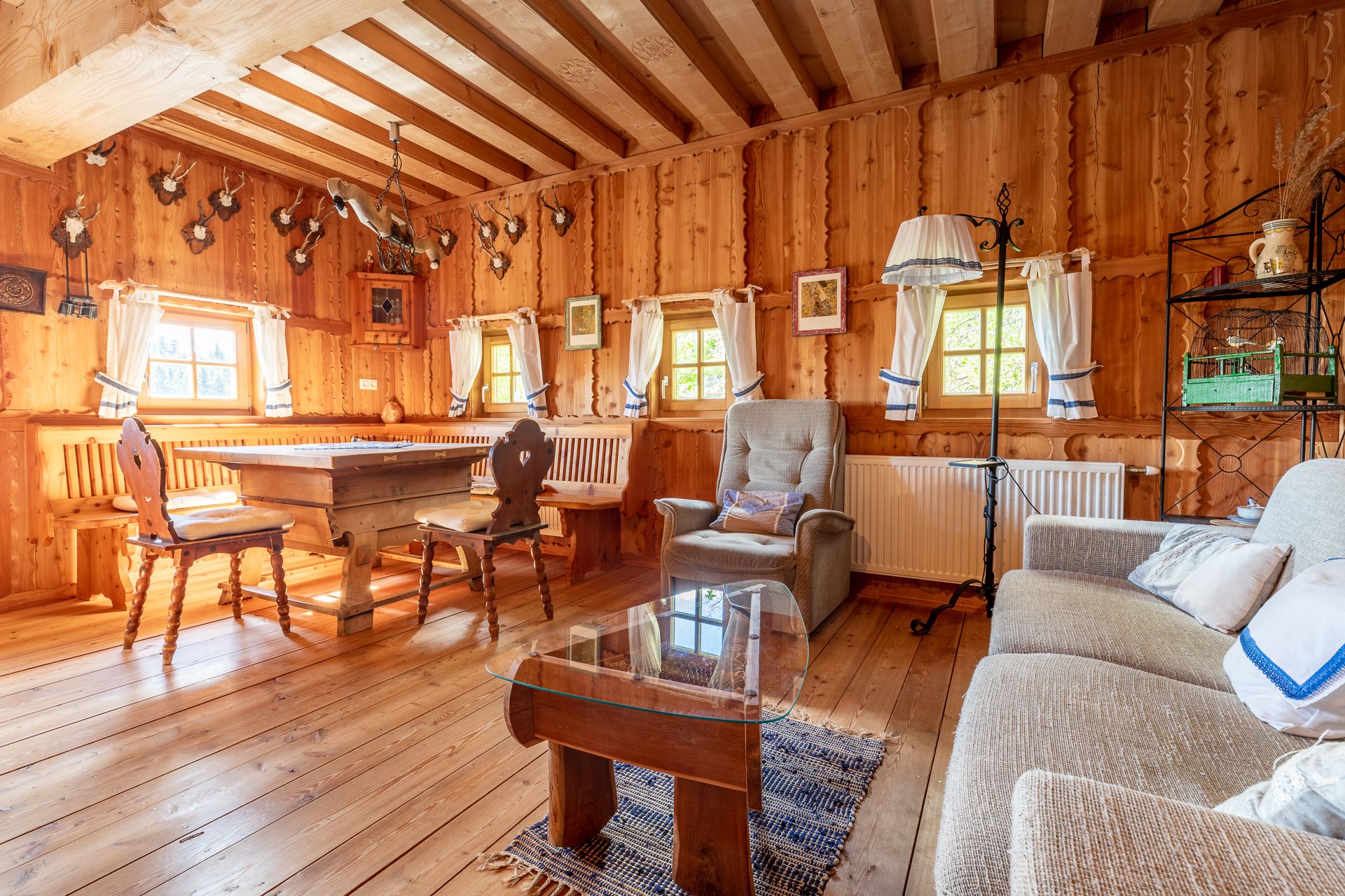 Rustic living and dining area with wooden furniture, wooden walls and hunting trophies on the wall.