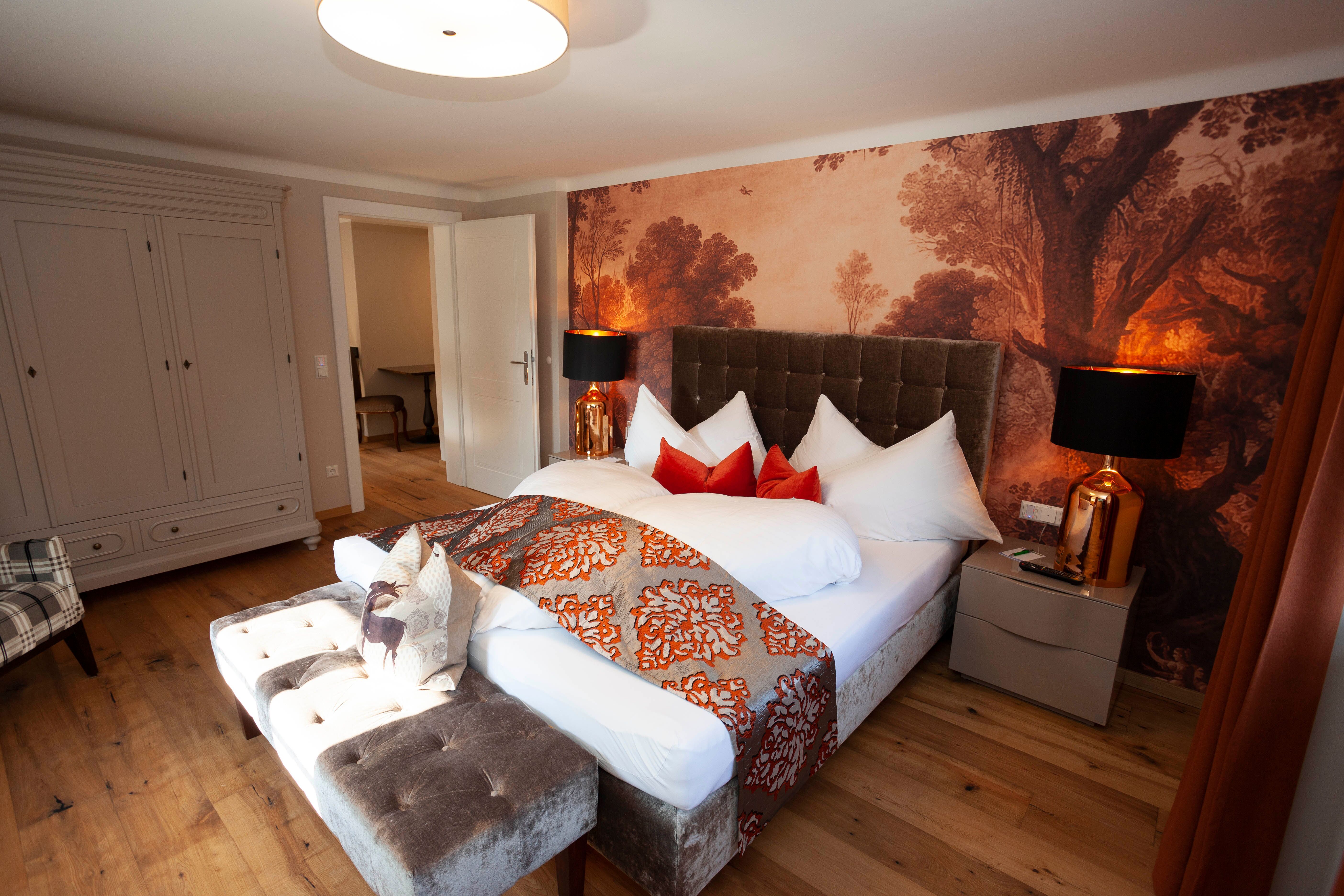 Elegant suite with large bed, decorative pillows and stylish wallpaper in Schloss Luberegg.