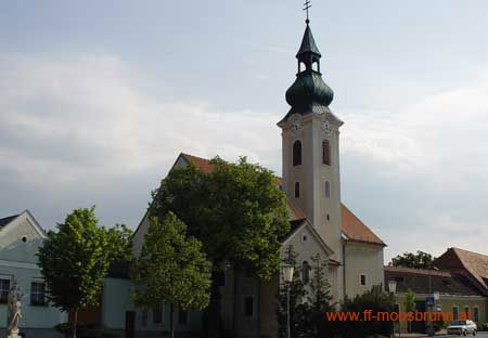 Church in Moosbrunn with green church tower and surrounding buildings.