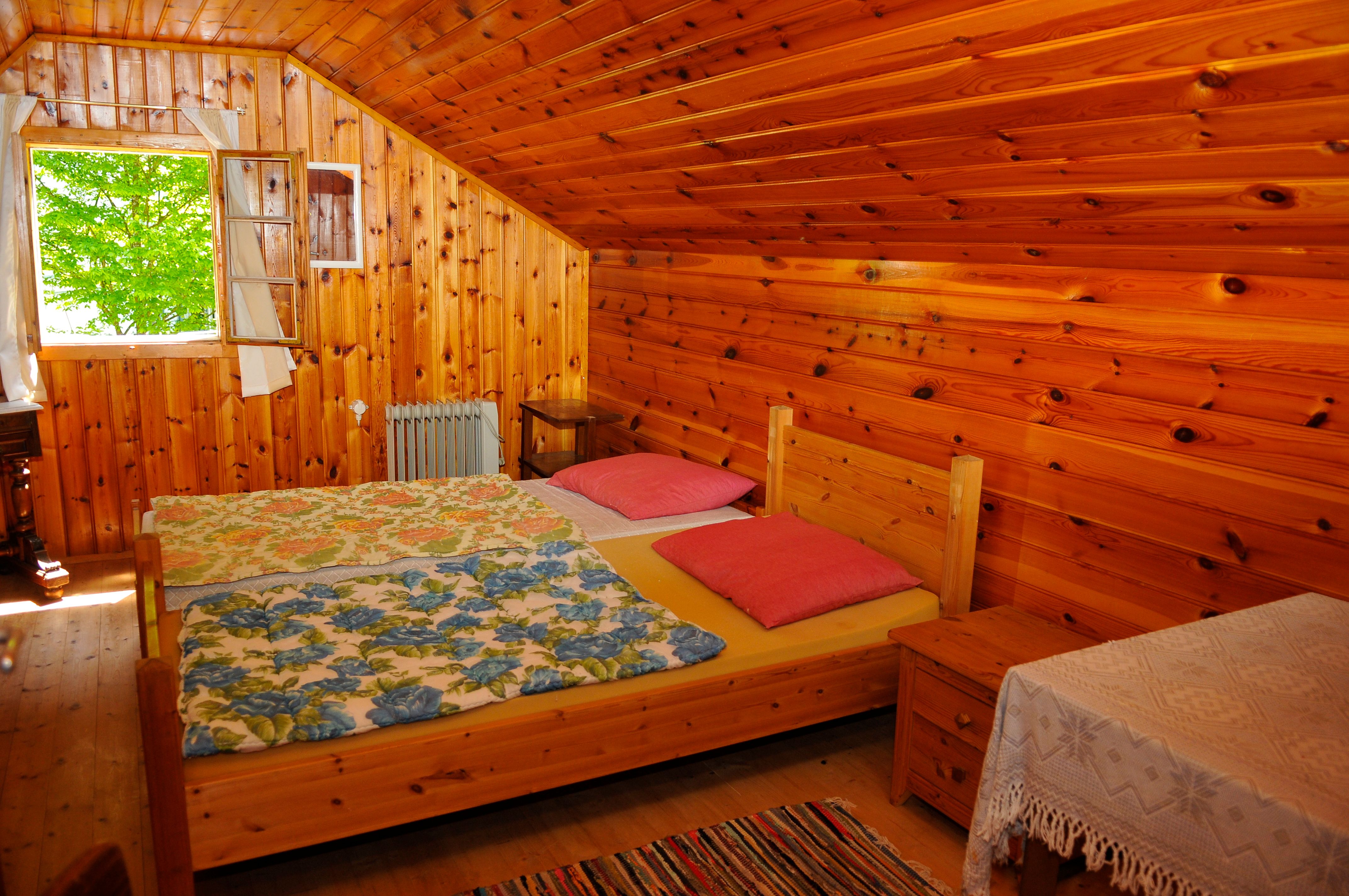 Wood-paneled bedroom with double bed, colorful blankets and open window.