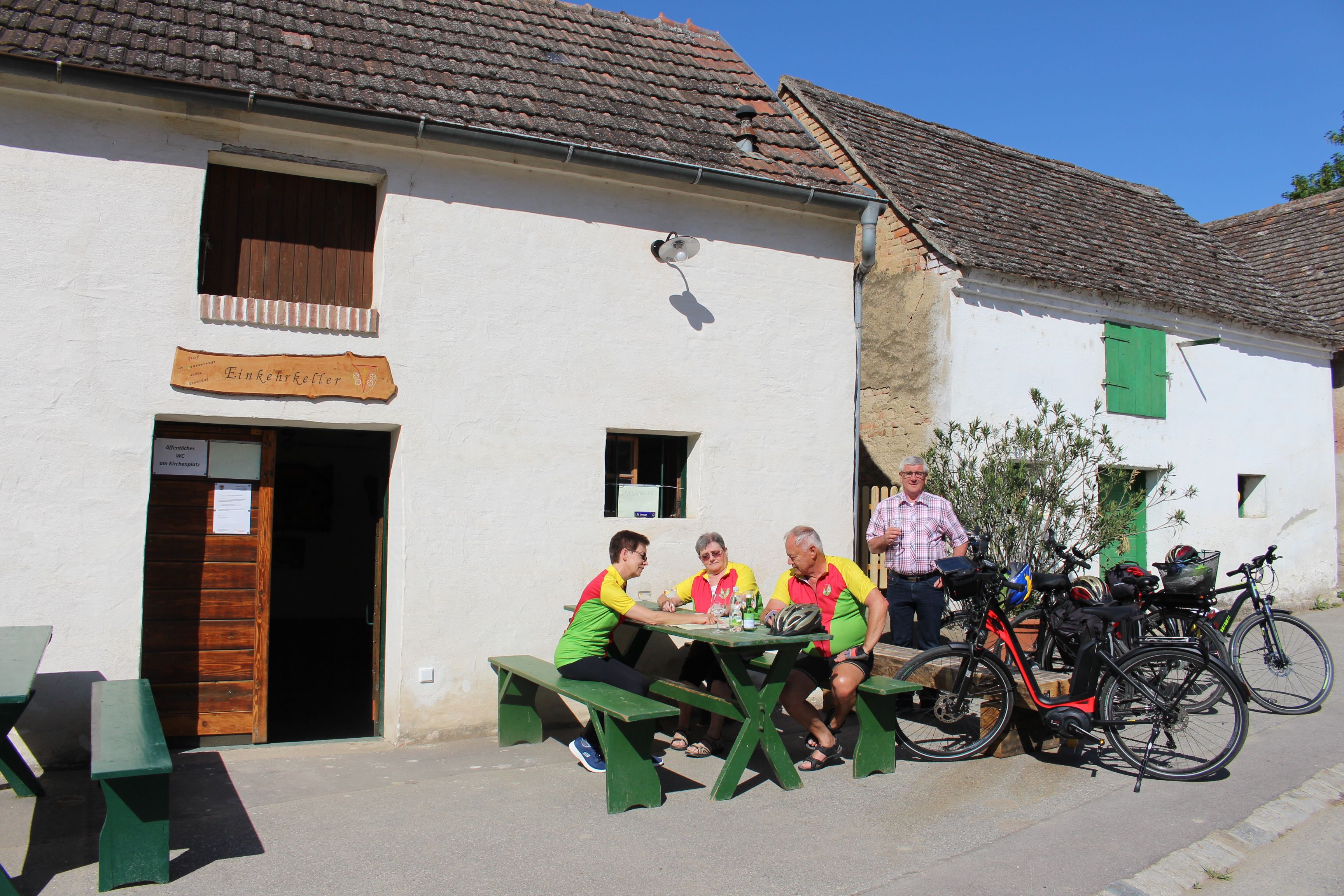 A group of people is sitting at a table in front of the Ottenthal restaurant. Bicycles are parked nearby. It is a sunny day.