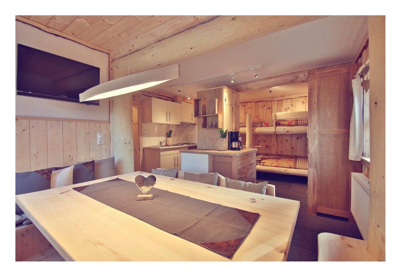 Interior view of a cozy chalet with wooden furniture, dining table, kitchen and bunk beds.