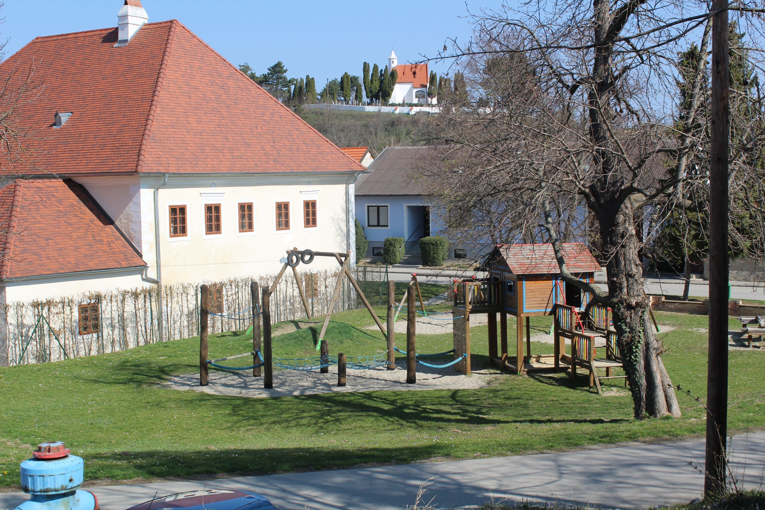 A children's playground with a climbing frame and swings next to a building with a red roof.