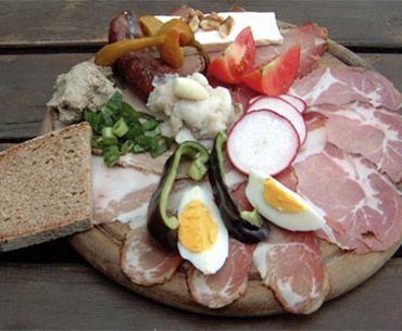 A traditional board with various types of sausage and cheese, bread, eggs and vegetables.