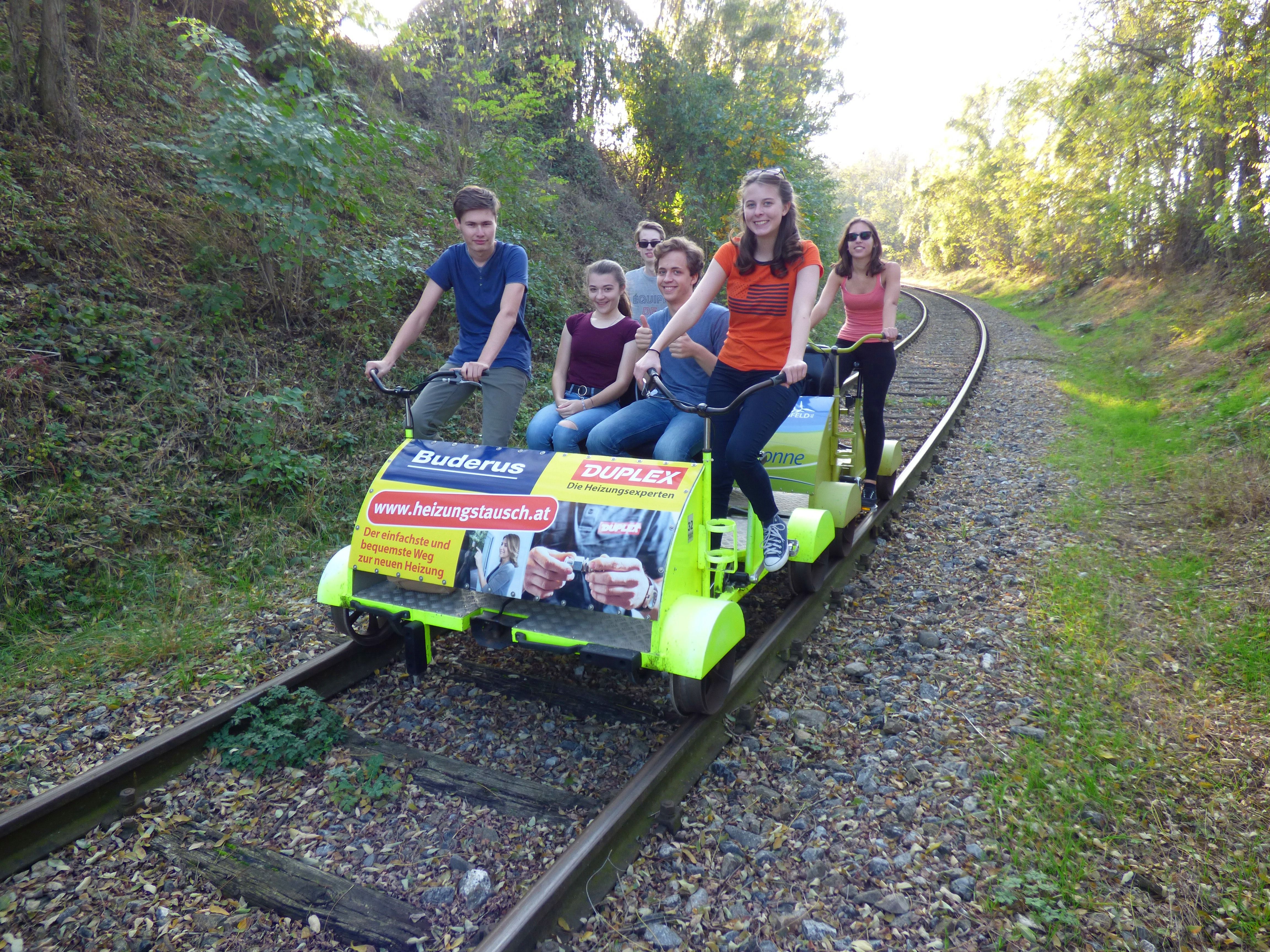 Group of people riding a trolley on railroad tracks through a wooded landscape.