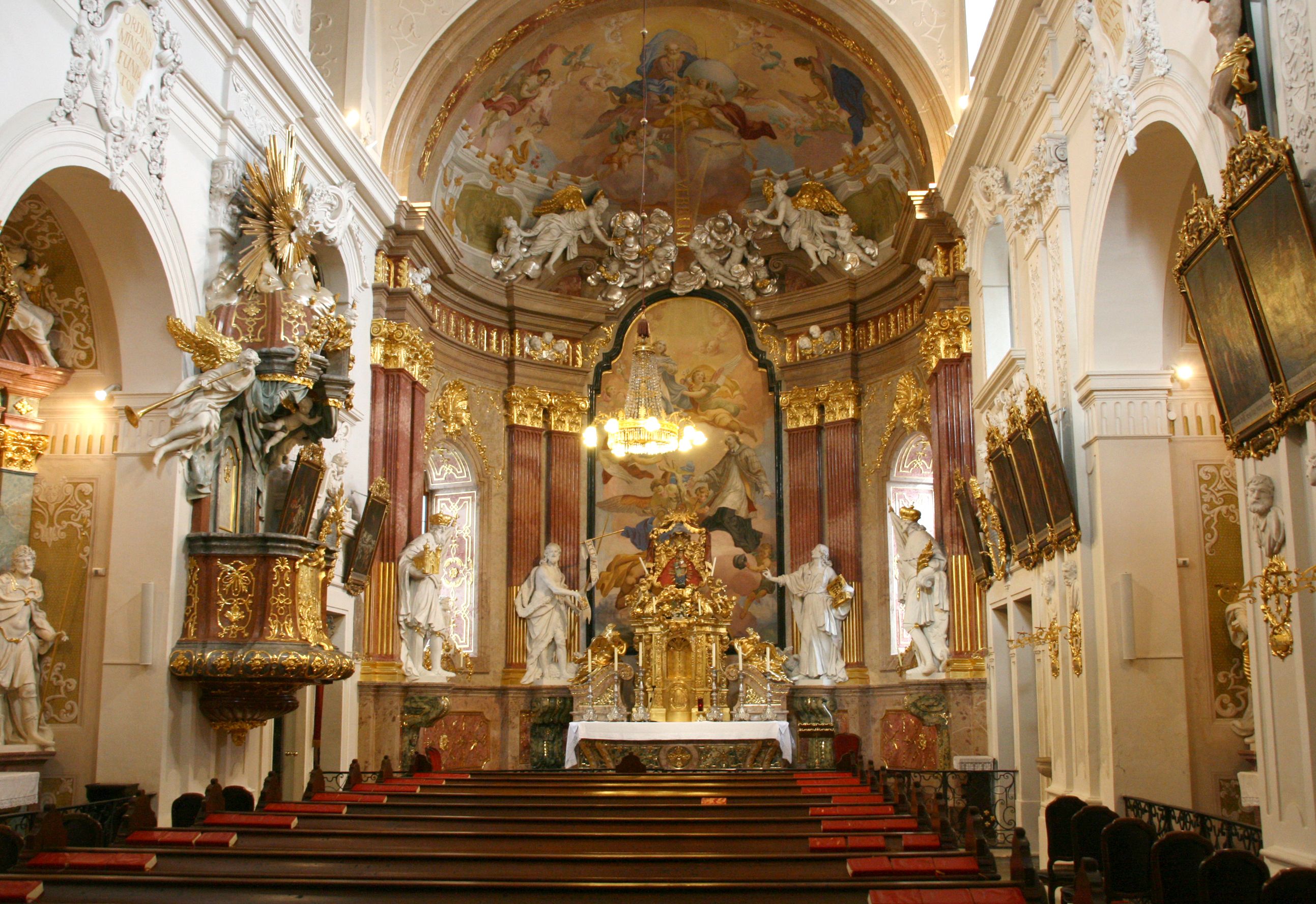Interior view of the Minorite Church with its richly decorated altar and ceiling frescoes.