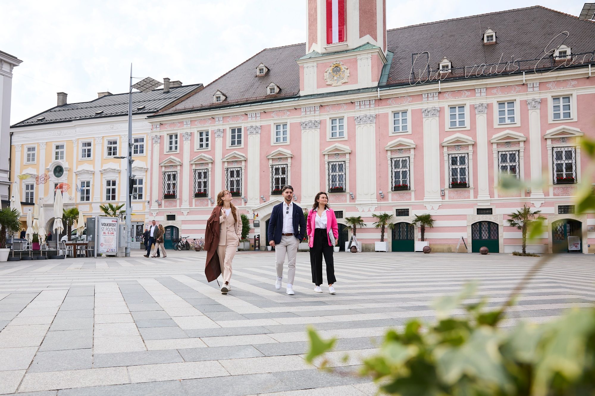 Three people in business outfits in front of the baroque town hall of St. Poelten