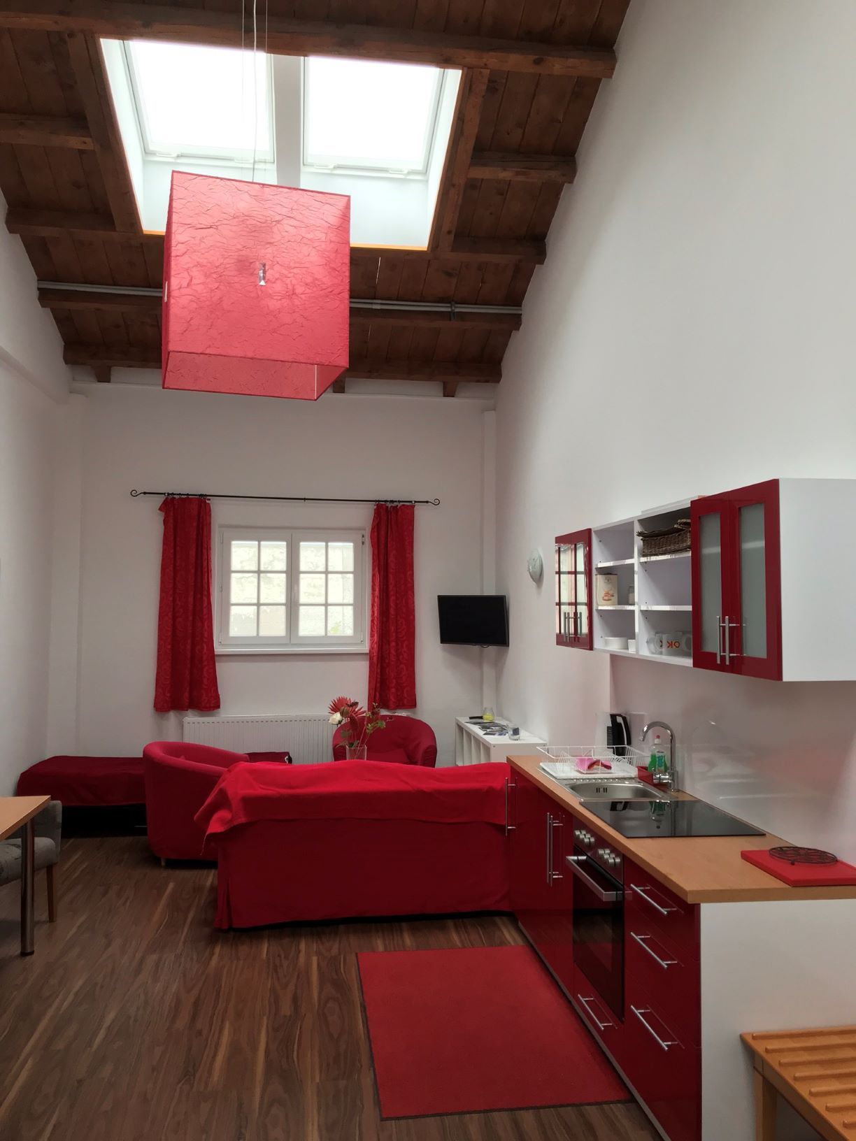 Living and dining area in a loft with red furniture and wooden beamed ceiling.