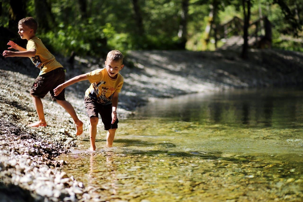 Two children play in nature on the banks of clear water.