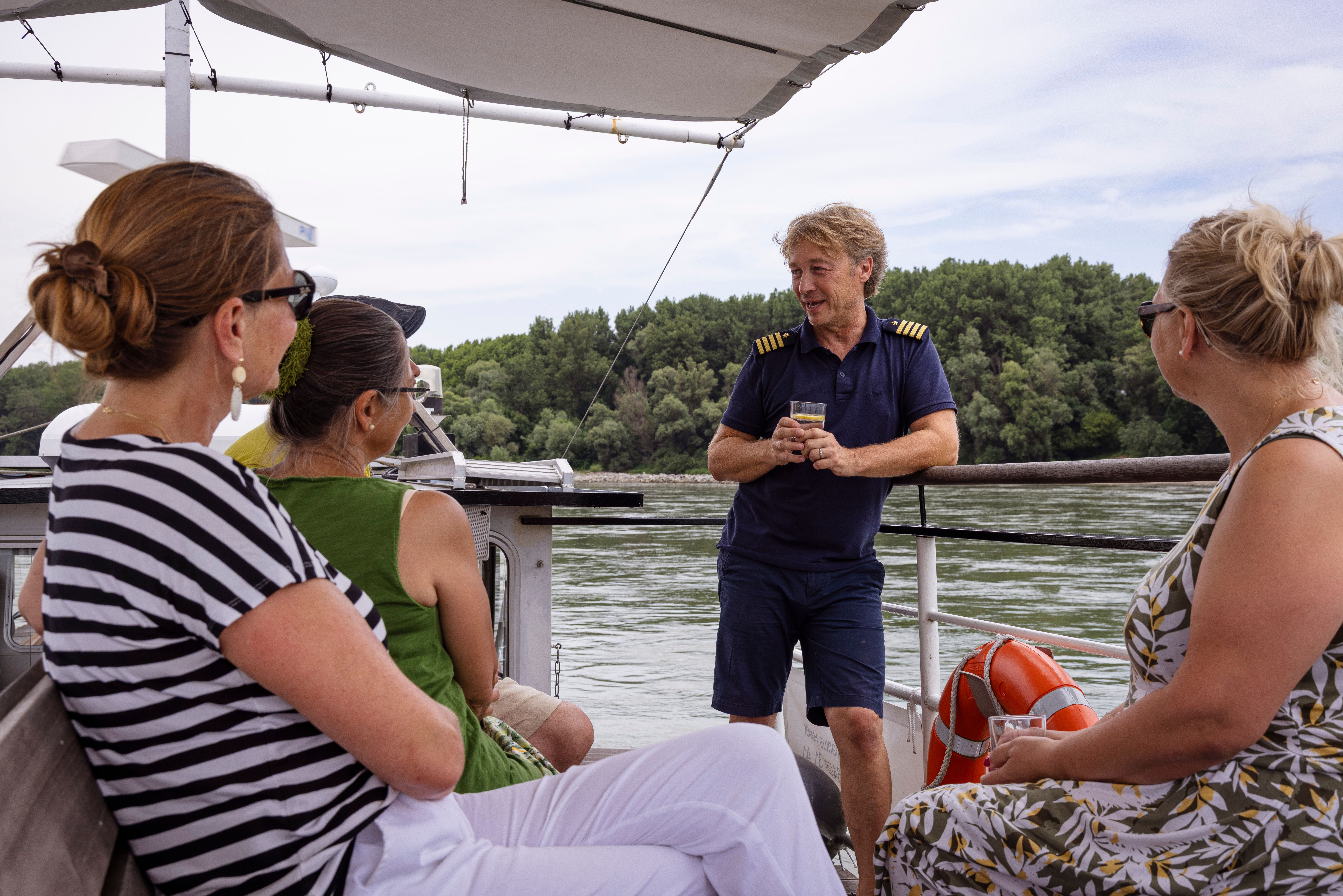 People on a boat on the Danube, a man in uniform (captain) talks to three women.