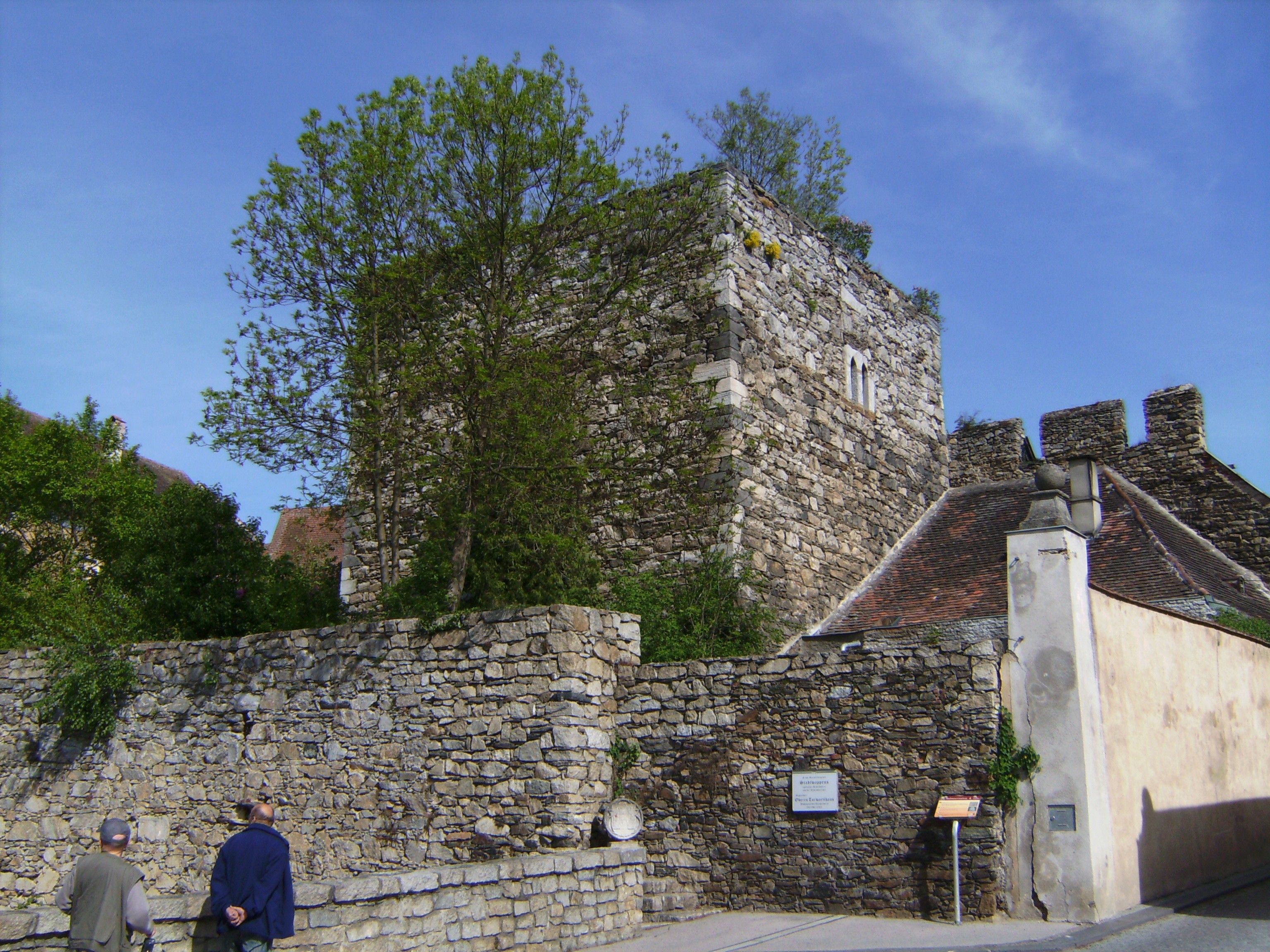 Historic stone wall and tower in Drosendorf-Zissersdorf, surrounded by trees and blue sky.