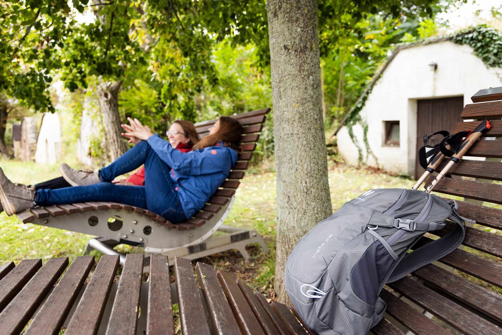 Two women on a wooden lounger, a hiking rucksack and old wine cellars in the background. 