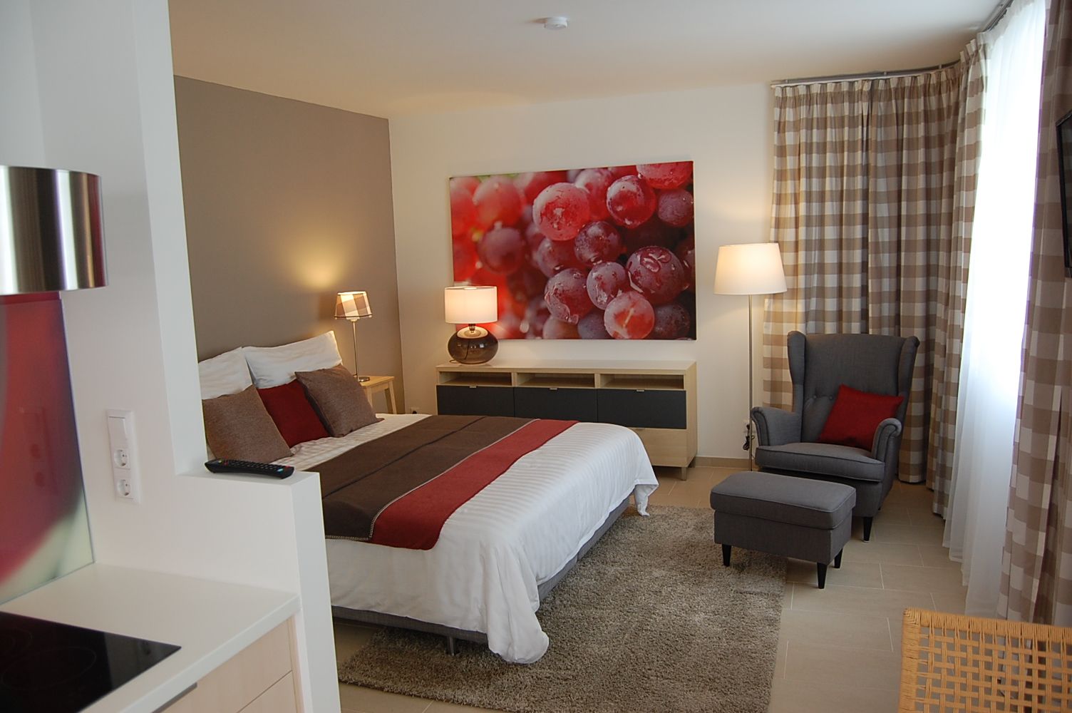 Modern bedroom with double bed, armchair and large picture of grapes on the wall.