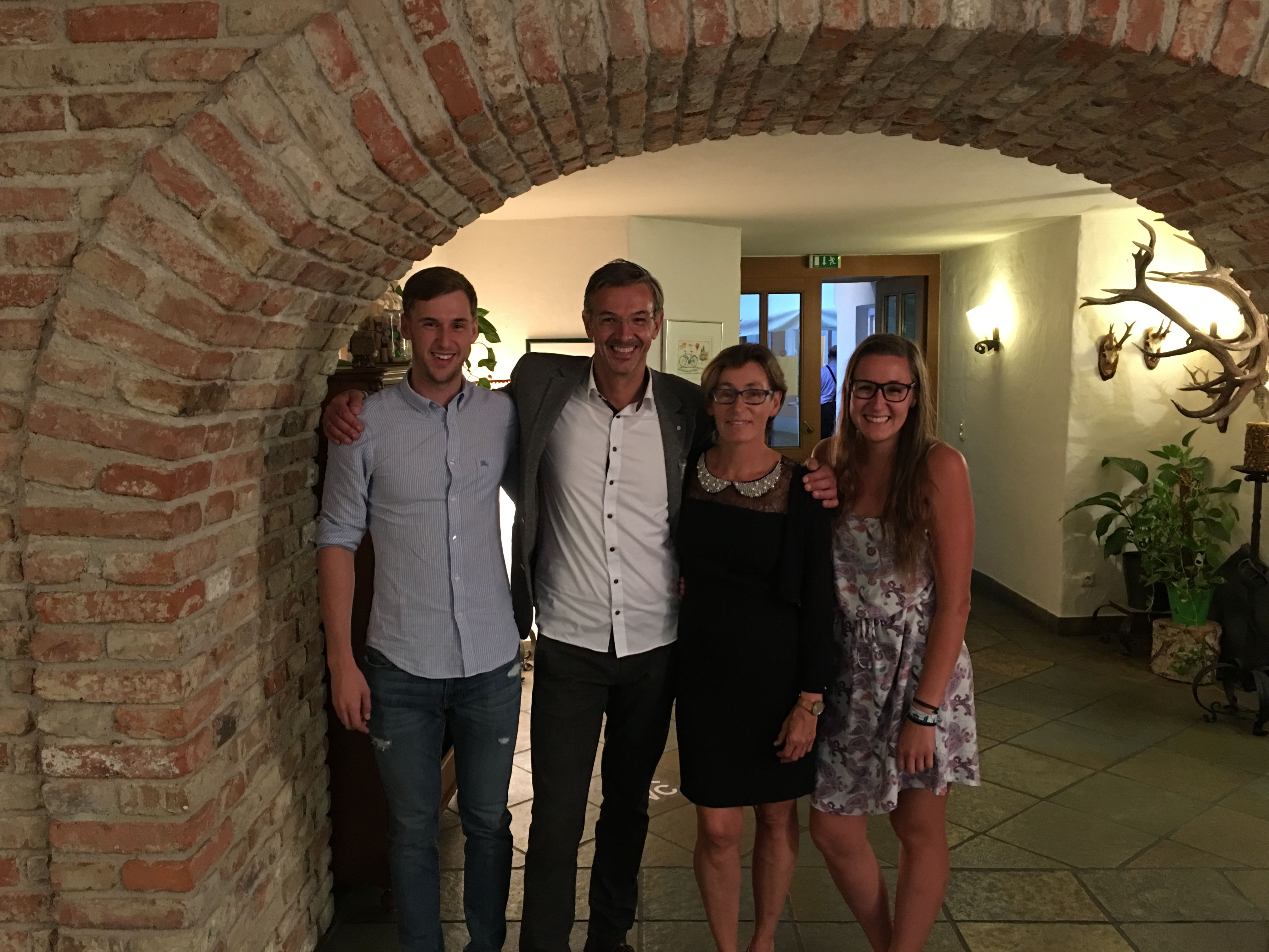 Four people stand smiling under a brick arch in a room with hunting trophies on the wall.
