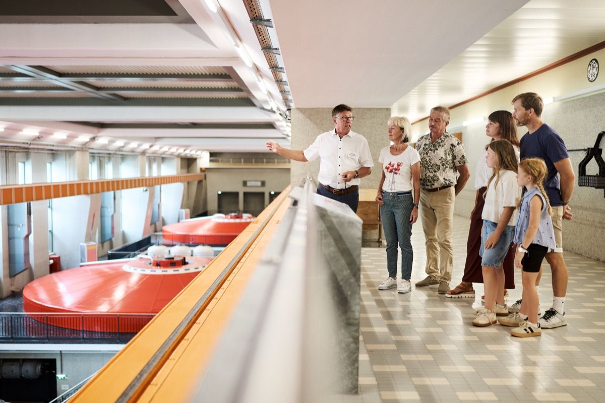 A tour guide with a group of visitors in the machine hall of the Ybbs-Persenbeug Danube Power Plant, explaining how hydroelectric power is generated.
