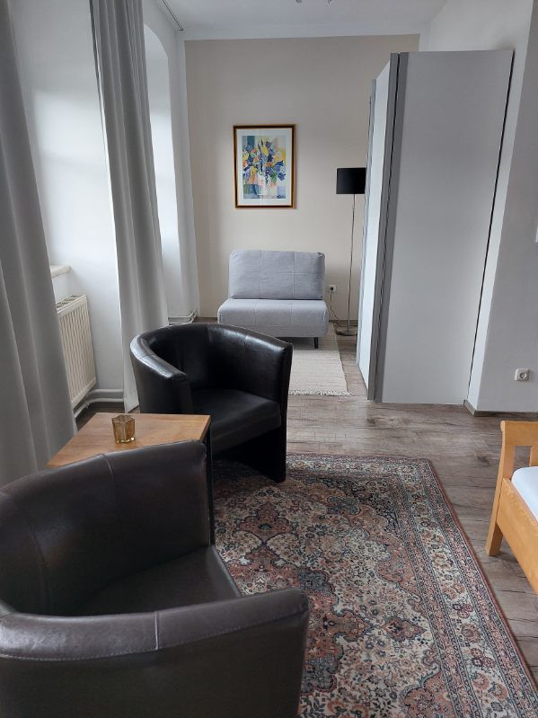 Modern guest room with two leather armchairs, carpet, gray armchair and artwork on the wall.