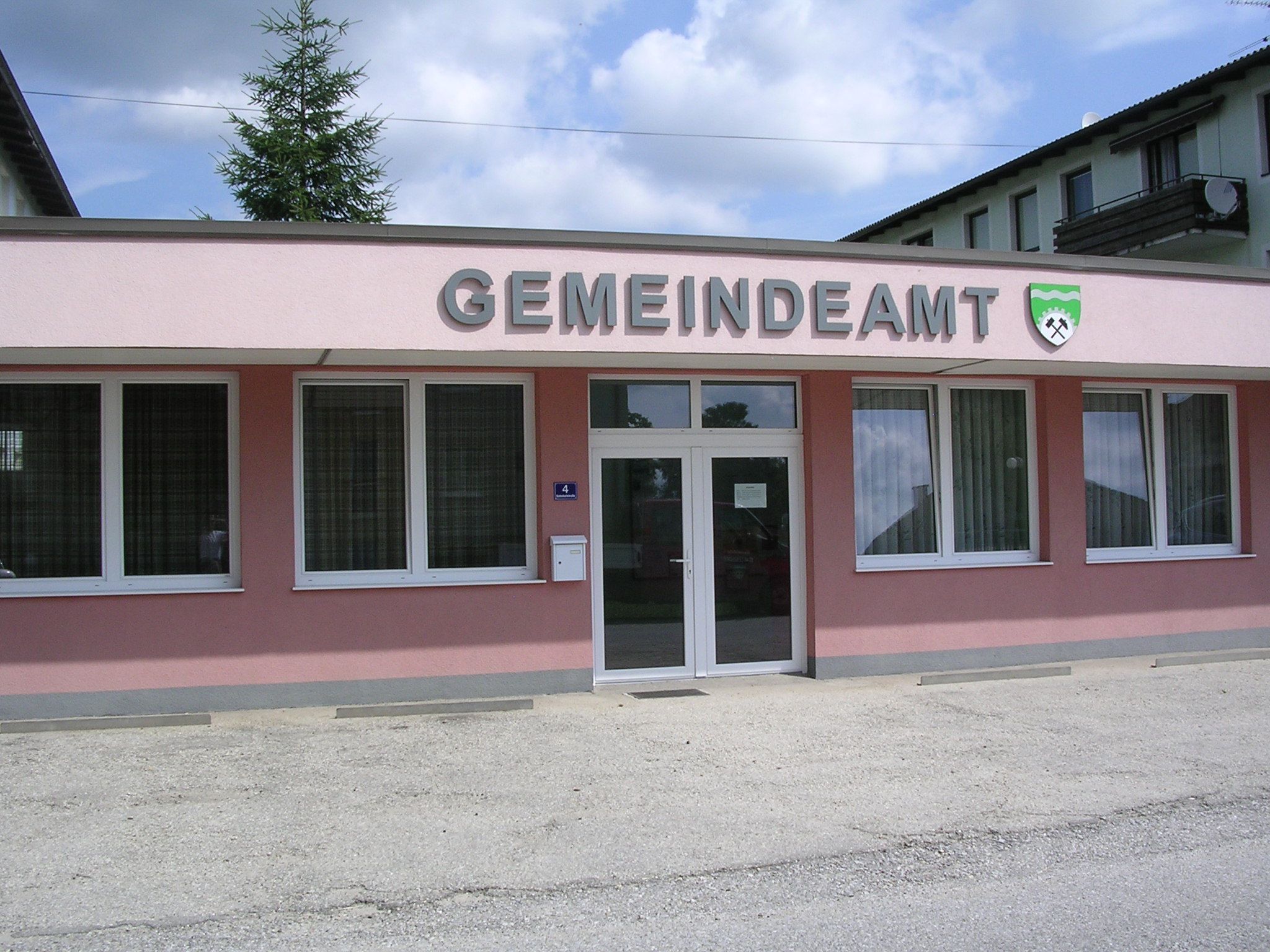 Exterior view of a pink building with the inscription 'GEMEINDEAMT' and a coat of arms.