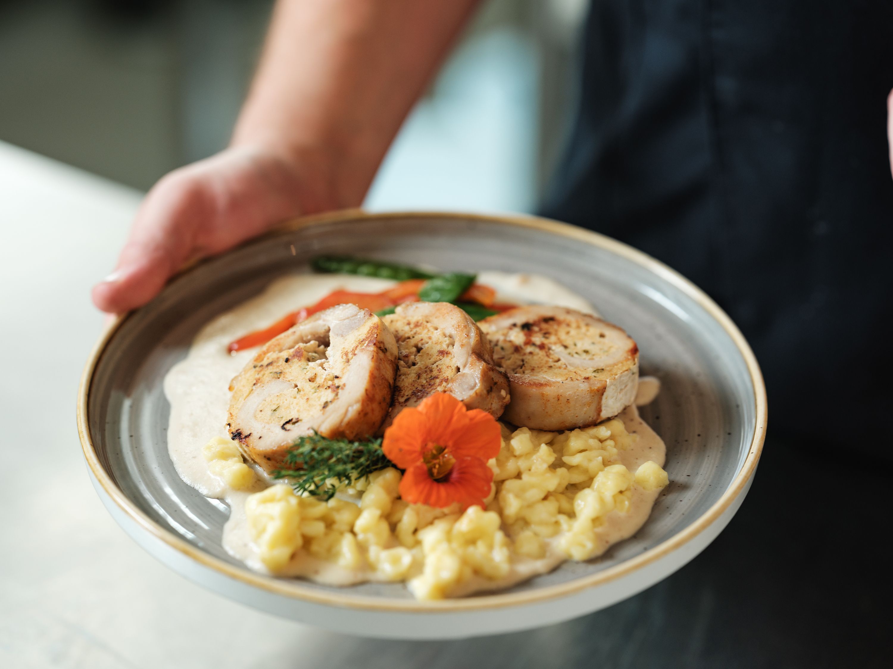 A plate with stuffed meat, spaetzle, vegetables and a flower as garnish.
