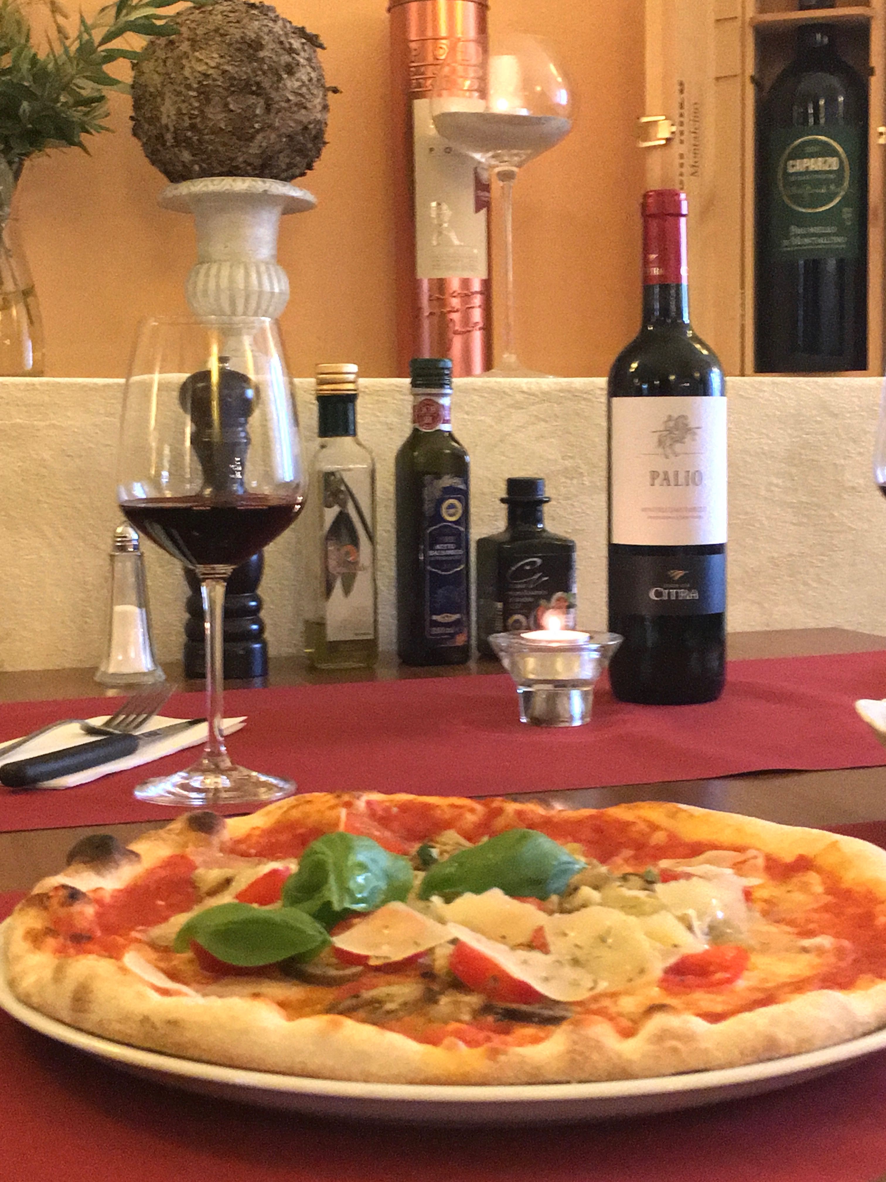 Pizza with basil and parmesan on a table with red wine and olive oil.