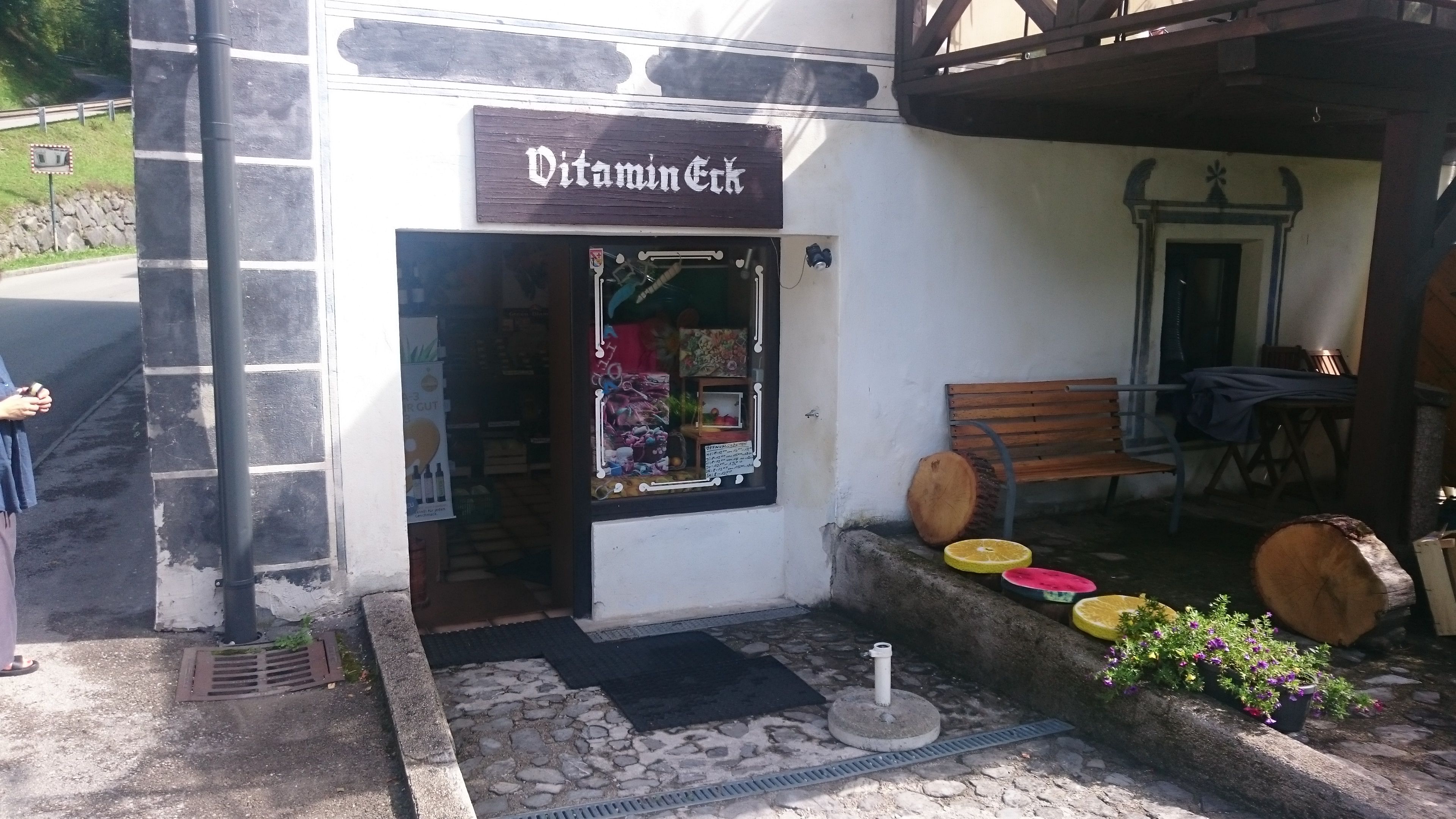 Entrance to a small store called Vitamin-Eck with a bench and decorations made of wood and flowers.