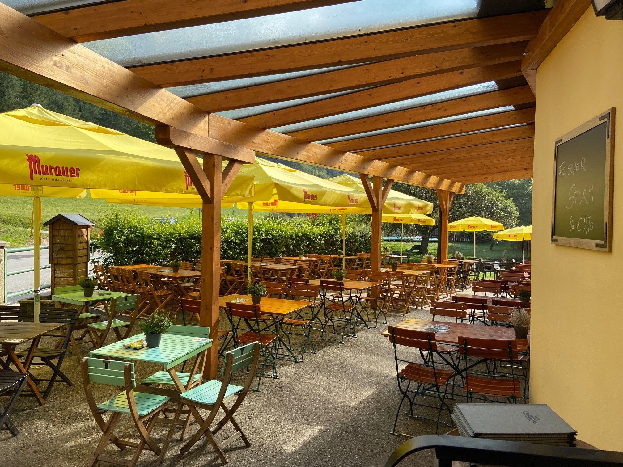 Covered terrace with wooden tables and yellow parasols at Gasthof Karnerwirt.