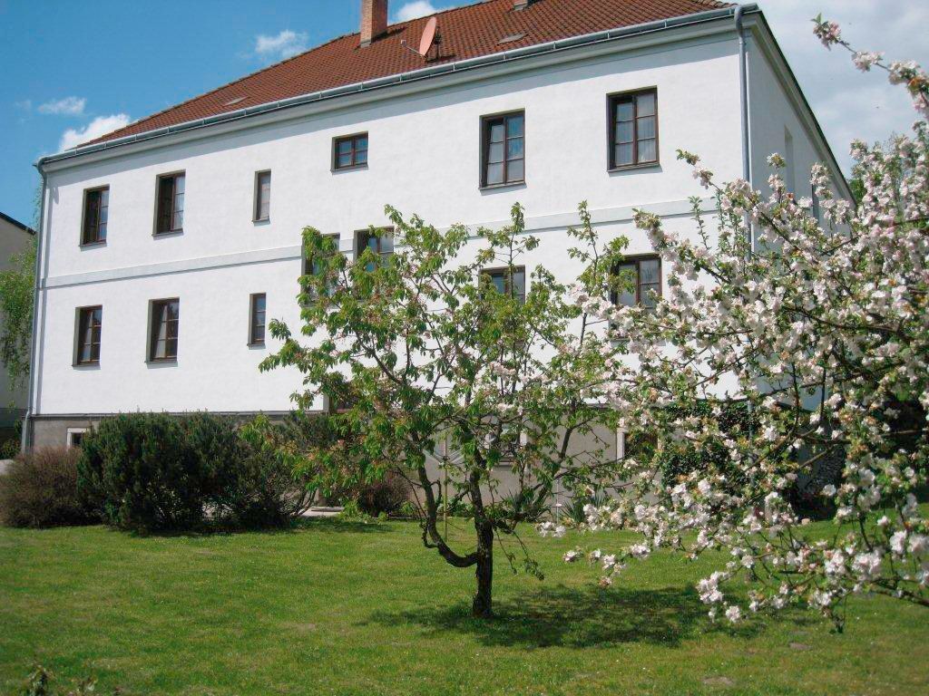 A white building with a brown roof and blossoming trees in the foreground.