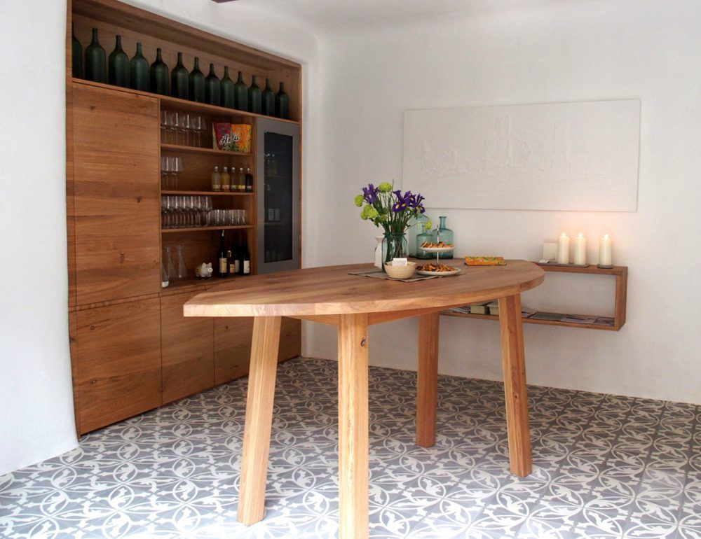 A stylish tasting room with a wooden table, shelves with bottles and glasses, flowers and candles.