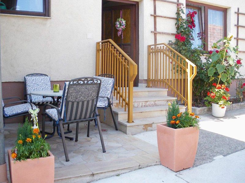 Entrance area of a vacation apartment with terrace, table and chairs, flowers and railings.