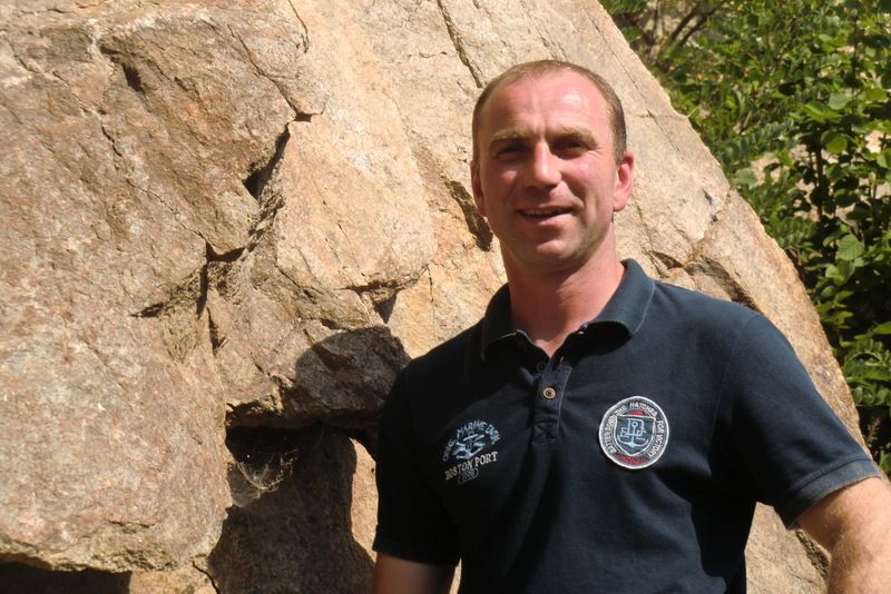 A man stands in front of a large rock and smiles at the camera.