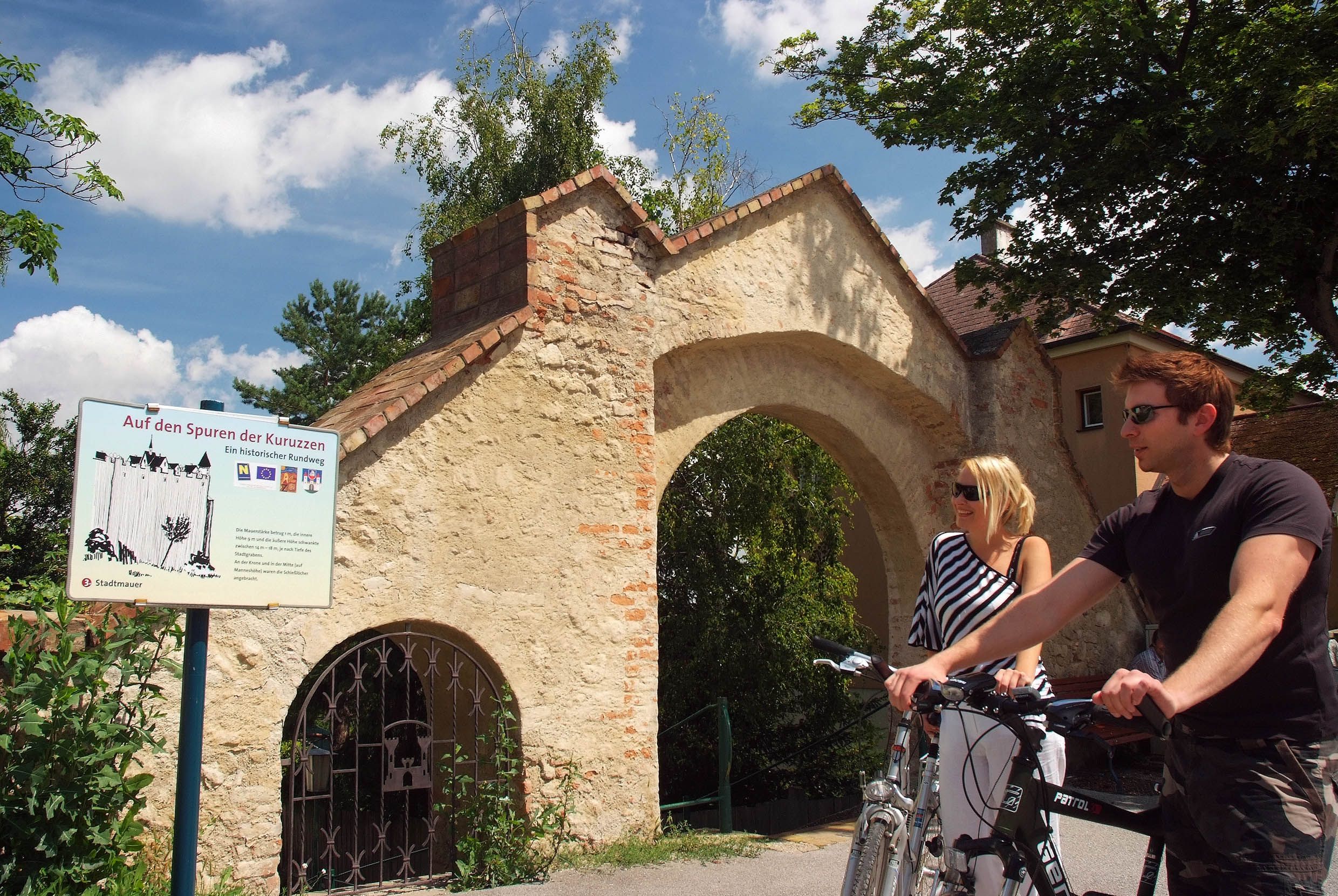 Two people with bicycles in front of a historic archway in Zistersdorf.