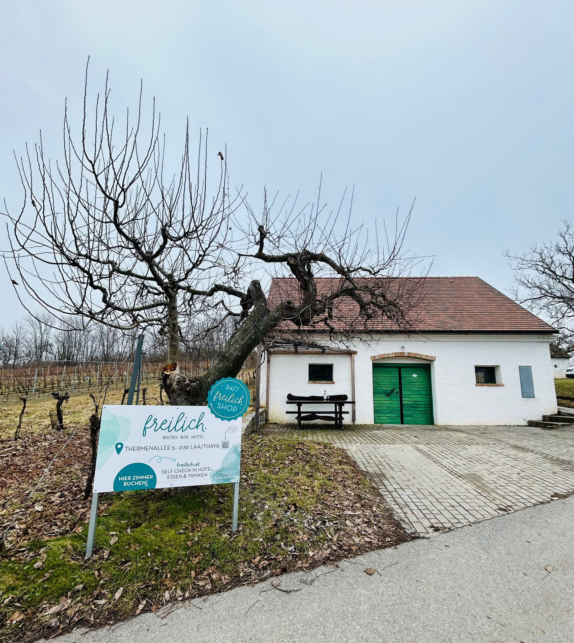 White building with green gate and sign 'freilich' in a rural setting.