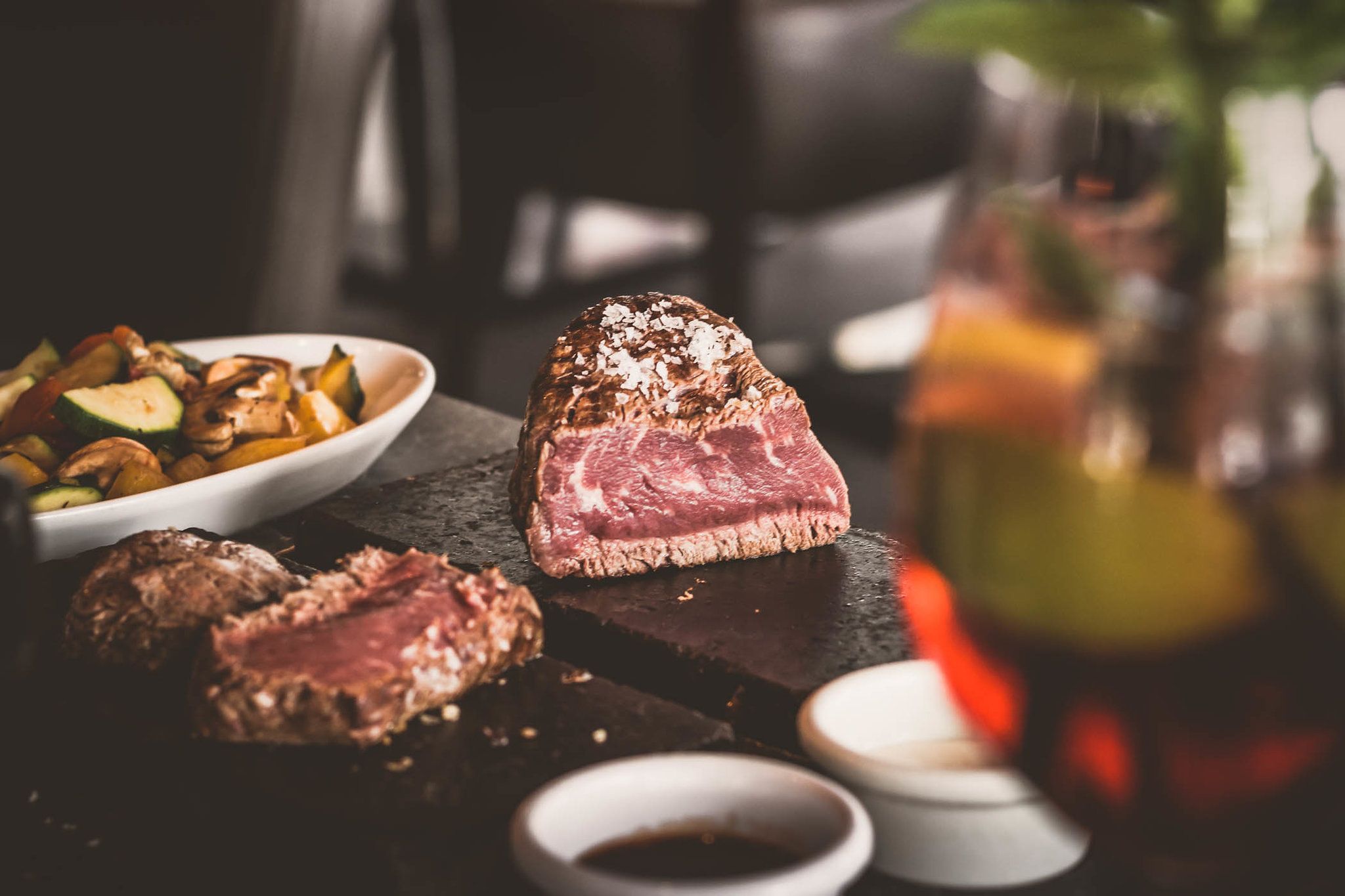 A juicy steak on a hot stone, accompanied by vegetables and sauces in small bowls.