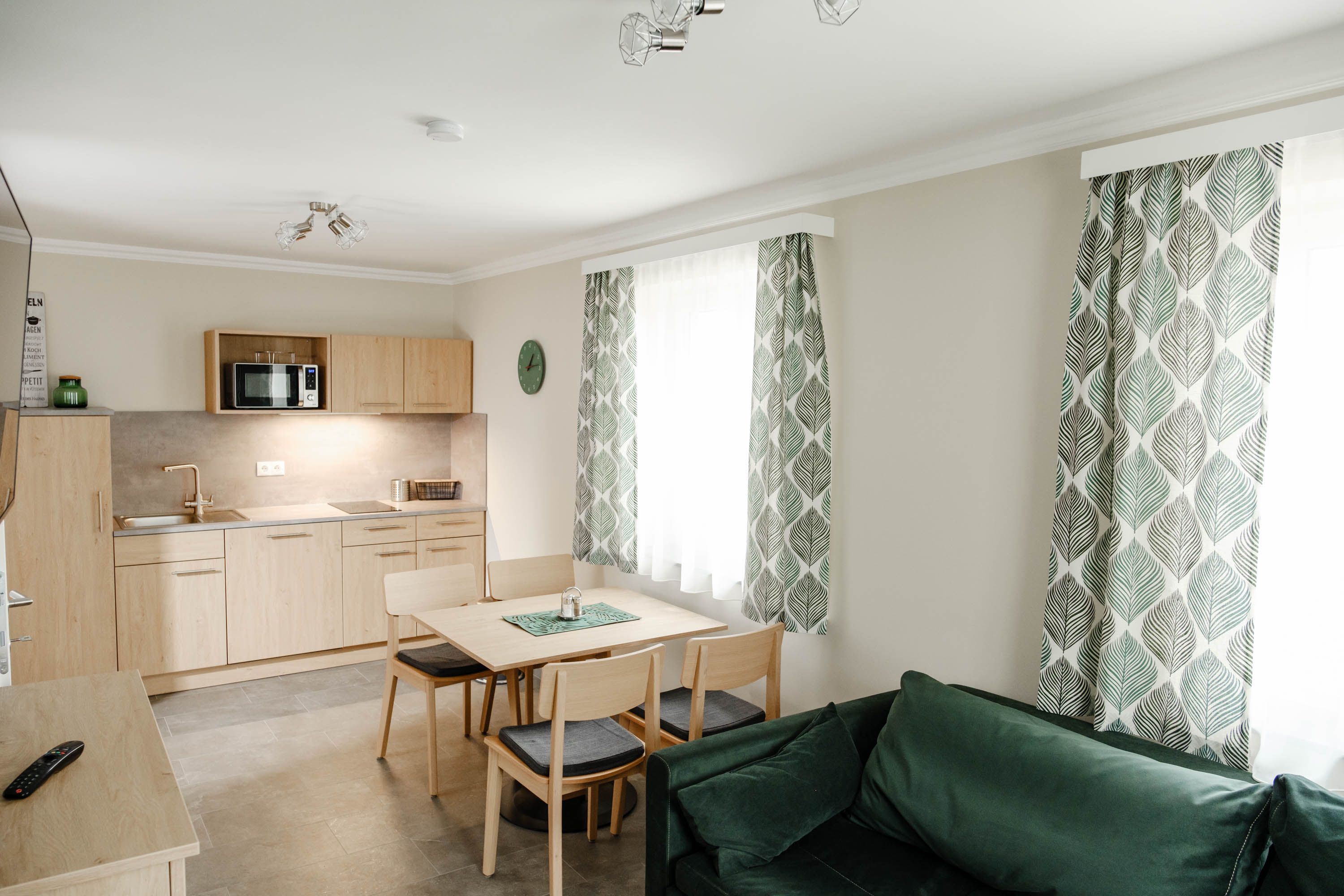 Modern kitchen with wooden furniture, dining table, green curtains and sofa.