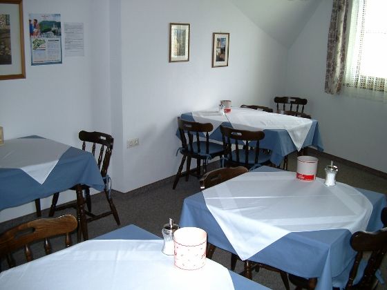 A breakfast room with several tables set with blue and white tablecloths.