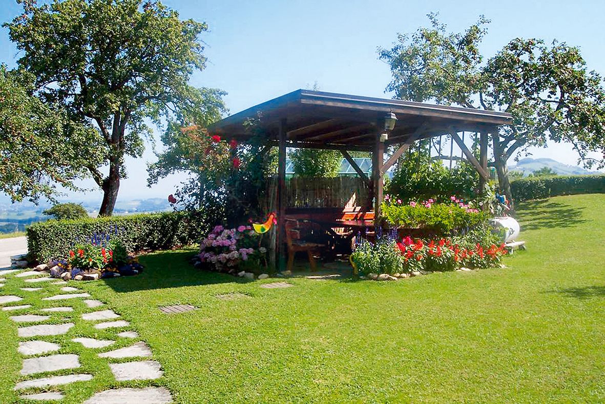 A pavilion on a green lawn with colorful flowers and trees in the background.