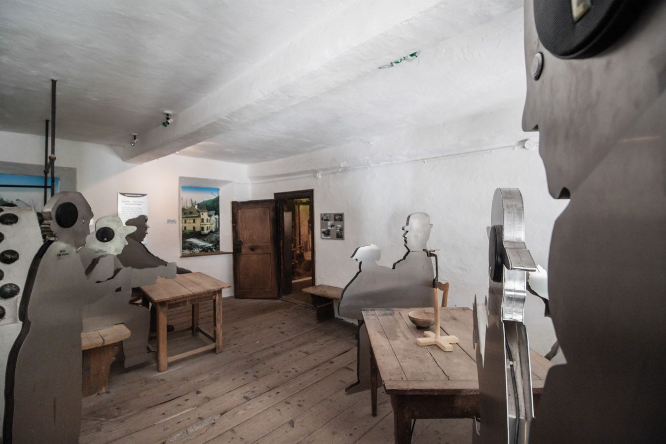 Interior with wooden floor and metal figures at wooden tables.