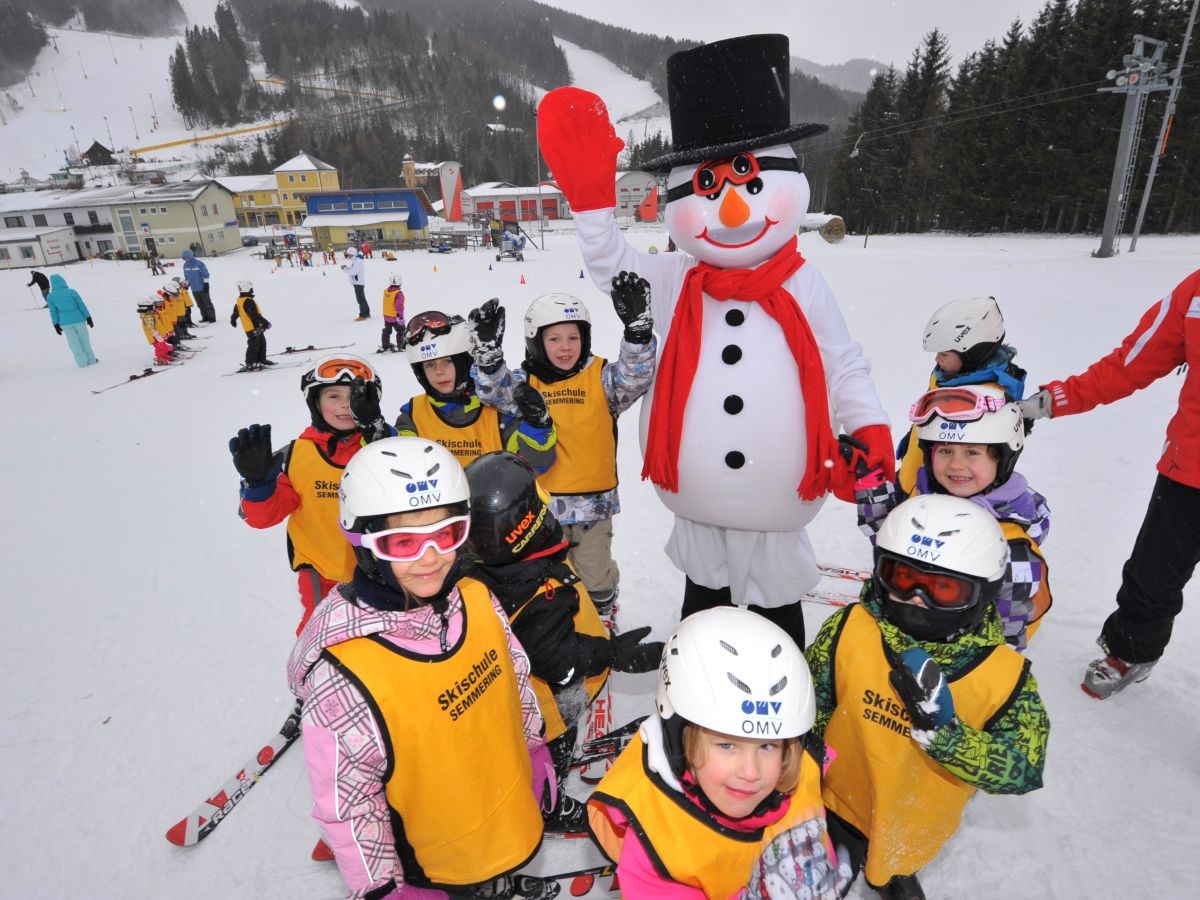 Children in ski equipment pose with a snowman on a ski slope.