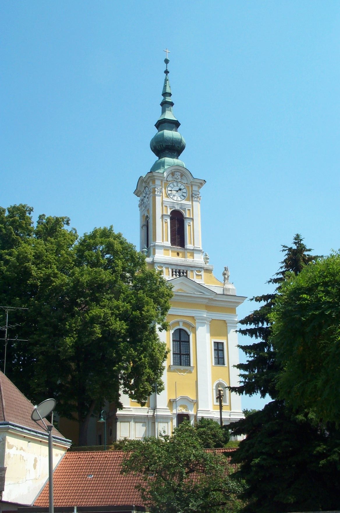 Yellow church with tower and clock in Groß-Siegharts, surrounded by trees.