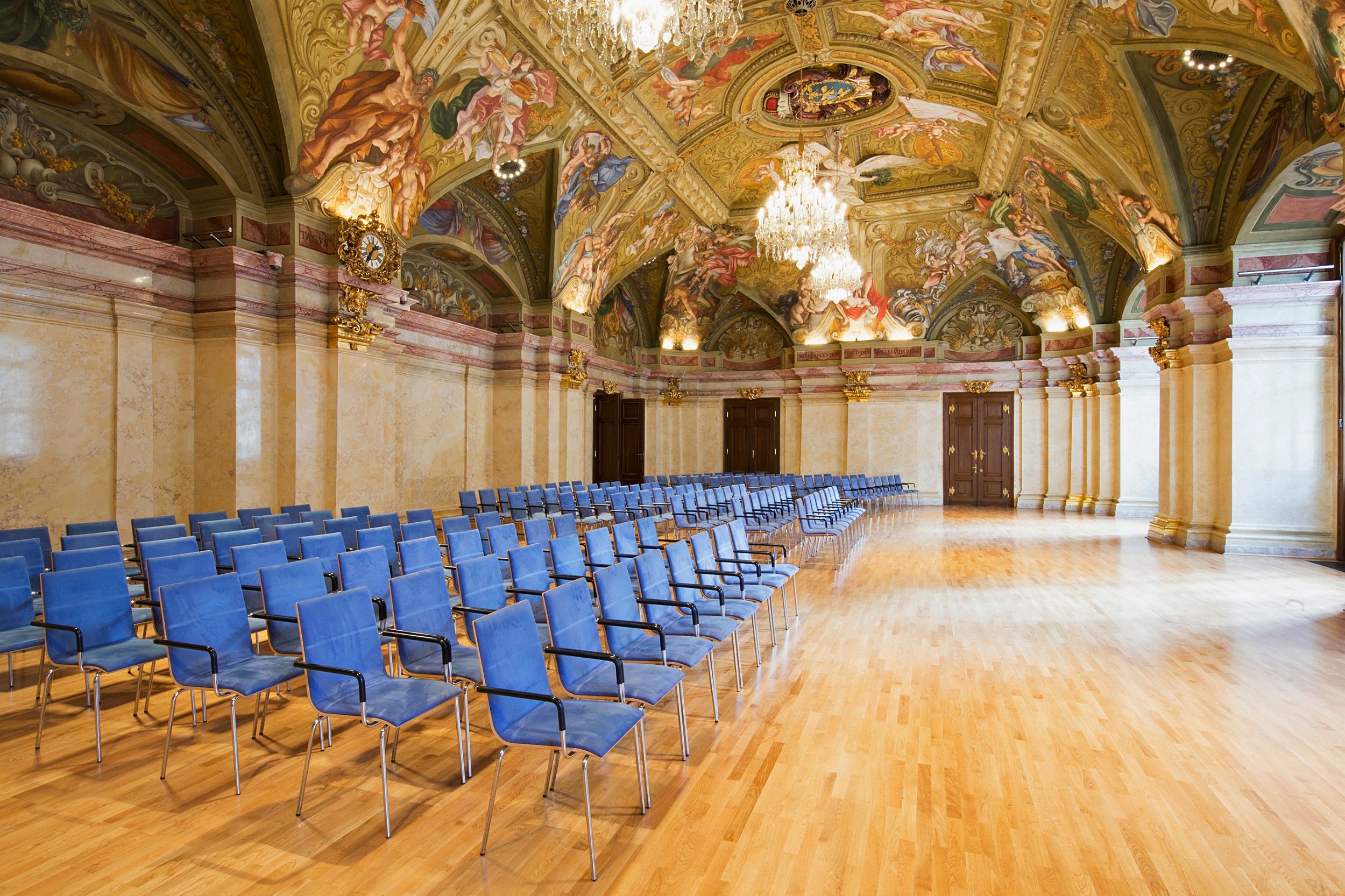 Interior view of the state parliament hall in the Palais Niederösterreich with blue chairs and artistically painted ceiling.