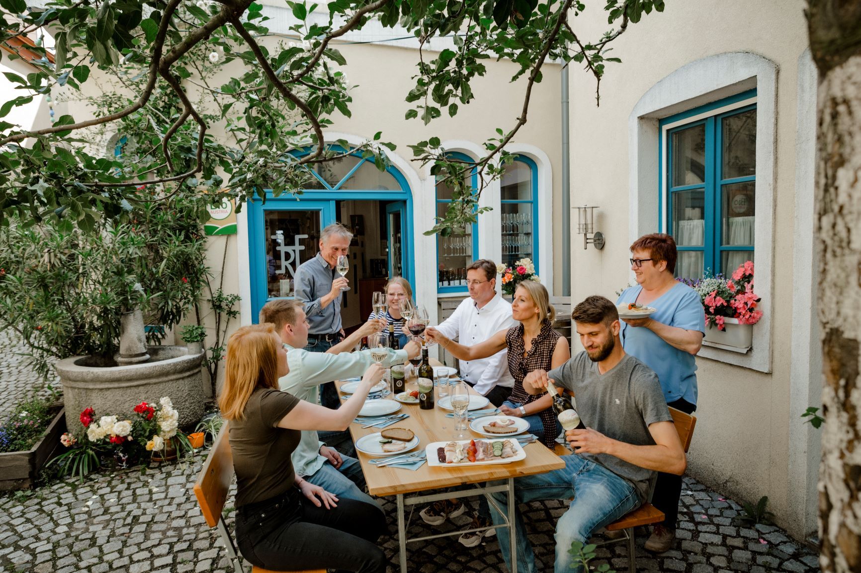 A group of people sit at an outdoor table and toast with drinks.