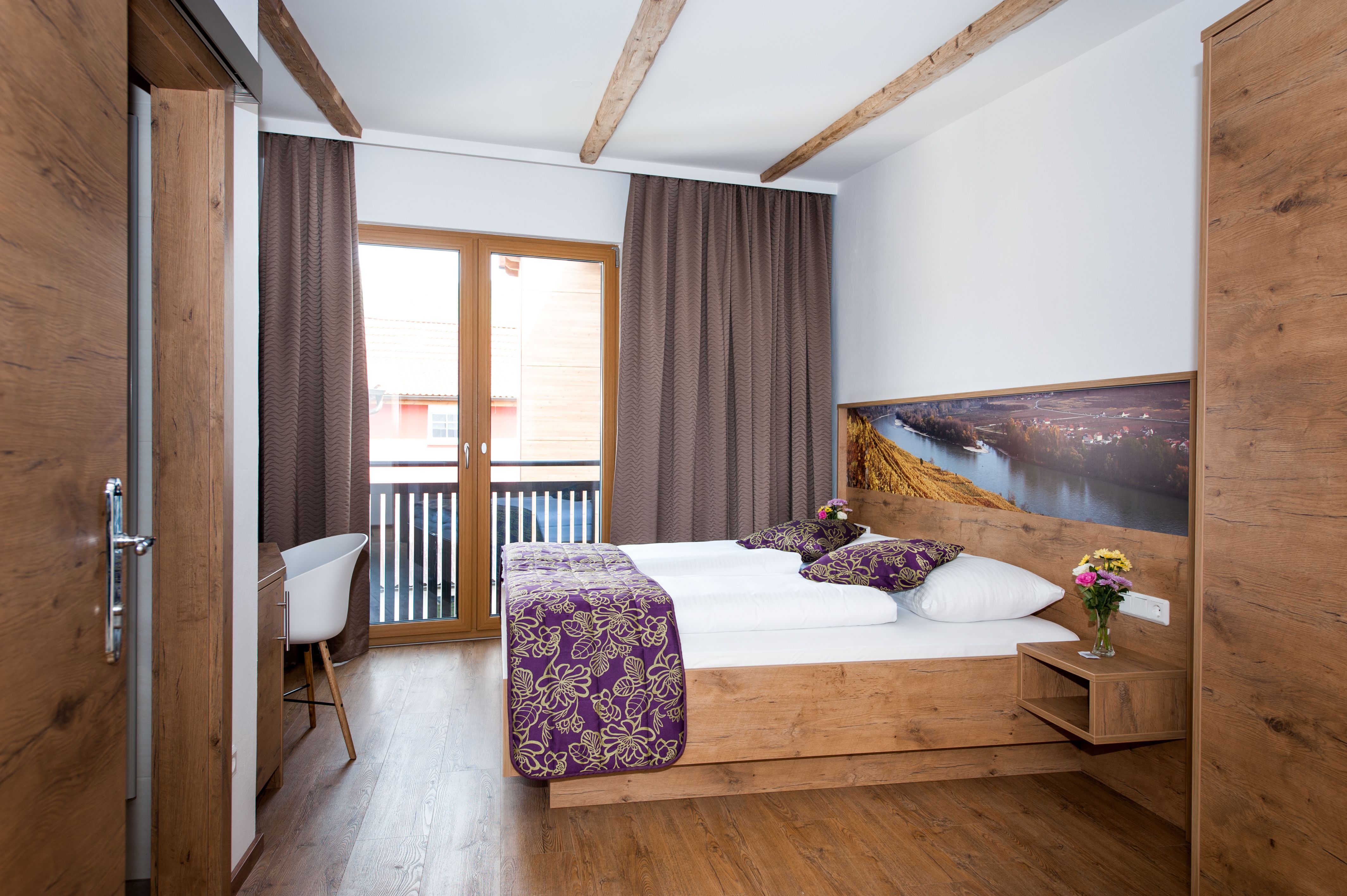 A cozy hotel room with wooden furniture, a double bed, balcony and decorative cushions.