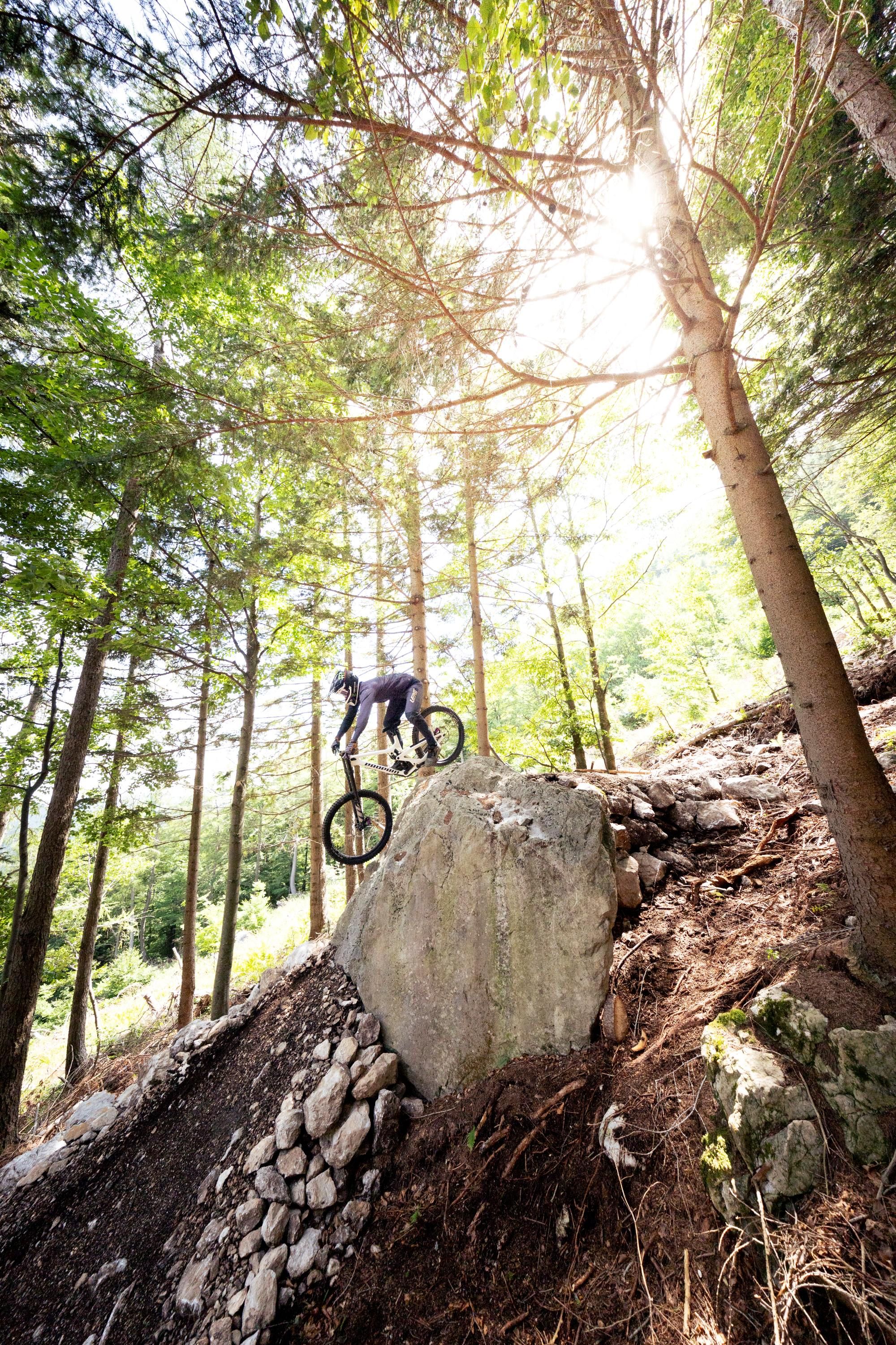 A mountain biker descends a steep cliff in the forest while the sun shines through the trees.