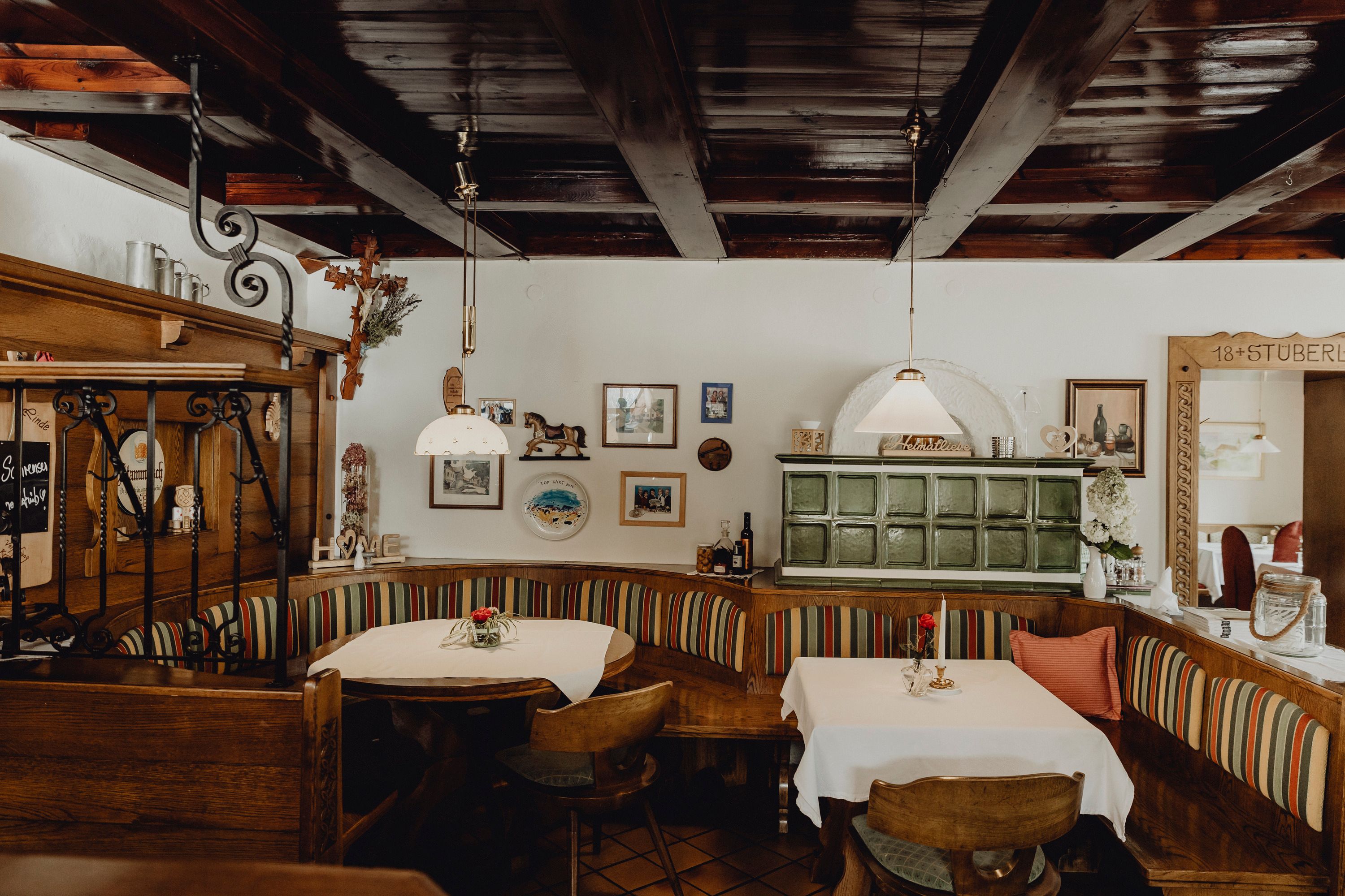 Cozy dining room with wooden furniture, tiled stove and decorative pictures on the wall.