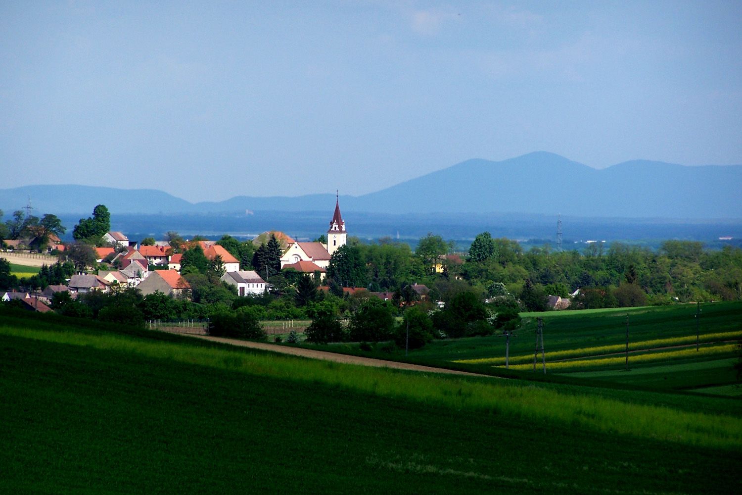 Landscape with village and church, surrounded by green fields and hills in the background.